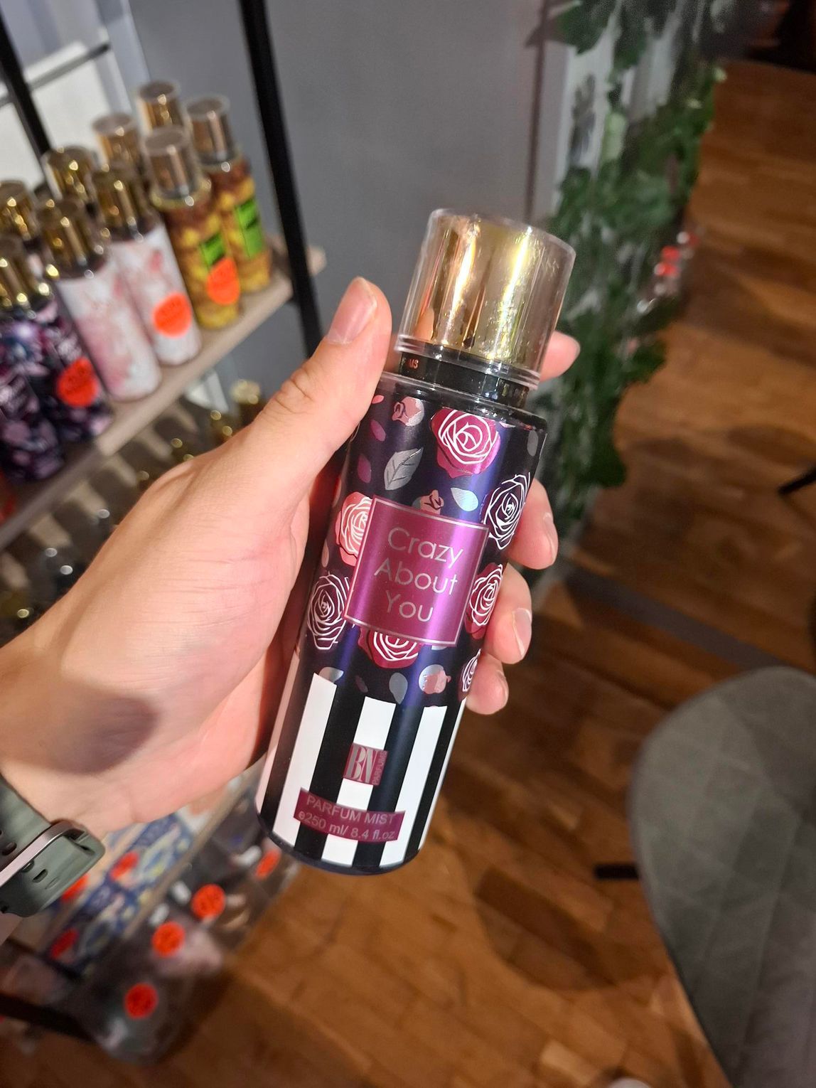 Een hand houdt een parfumverstuiver vast met een bloemenpatroon en zwarte en witte verticale strepen aan de onderkant.