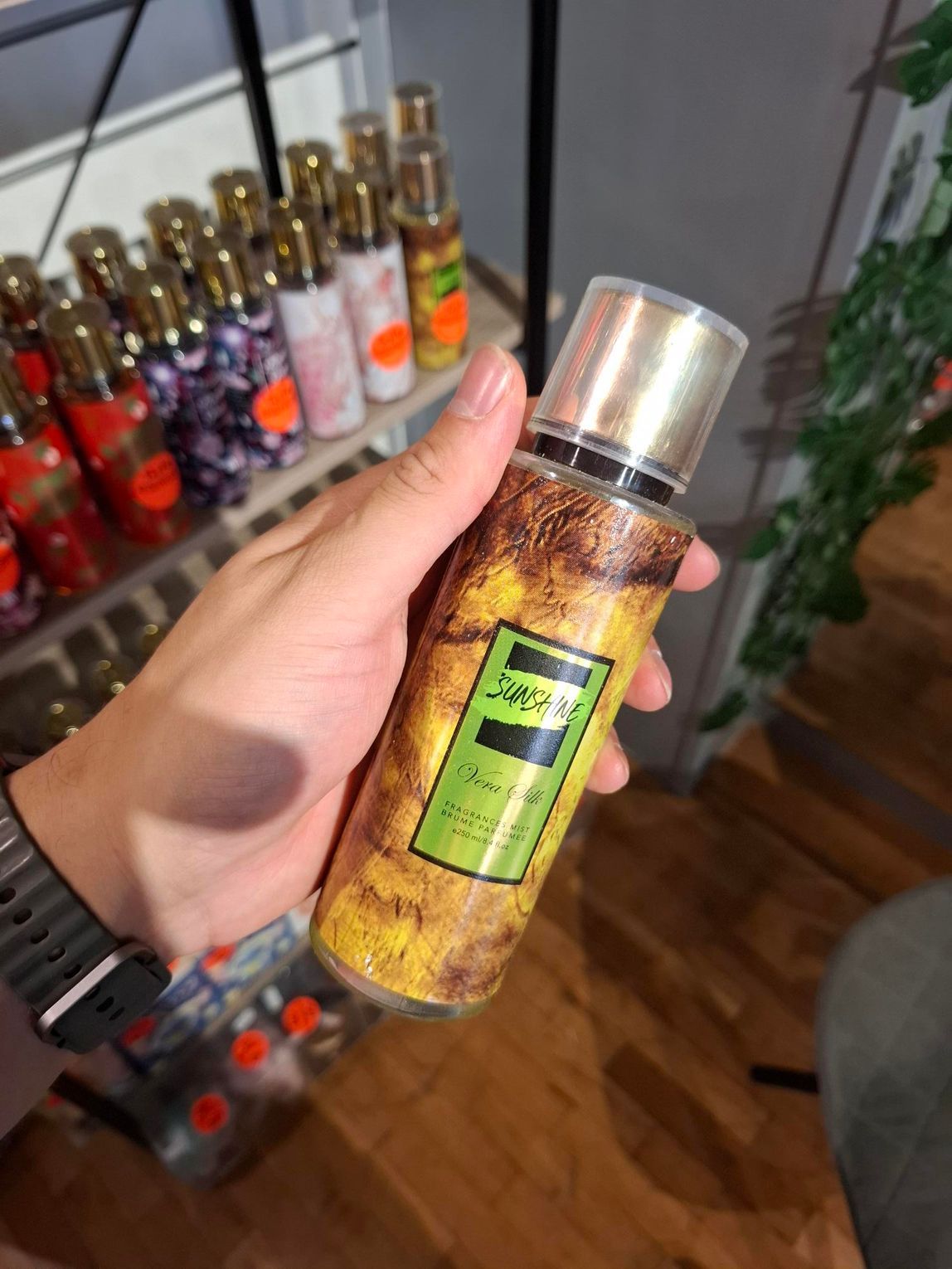Een hand houdt een geel Jaguar-parfumflesje vast voor een plank vol met verschillende geursprays.