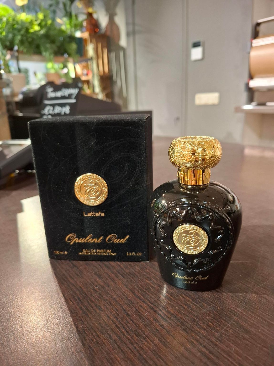 Een zwart parfumflesje met een sierlijke gouden dop en embleem, naast de bijpassende zwarte doos op een houten ondergrond.