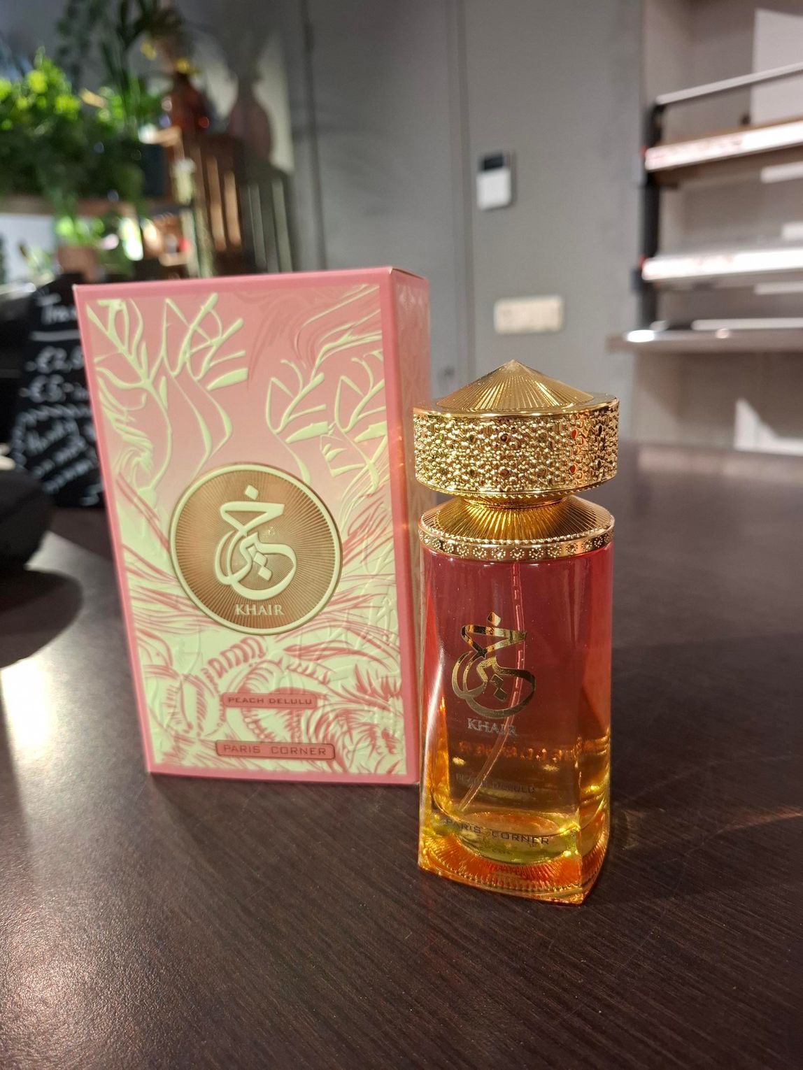 Op een houten tafel staan ​​een roze doos en een bijpassend glazen parfumflesje met een goudkleurige dop.