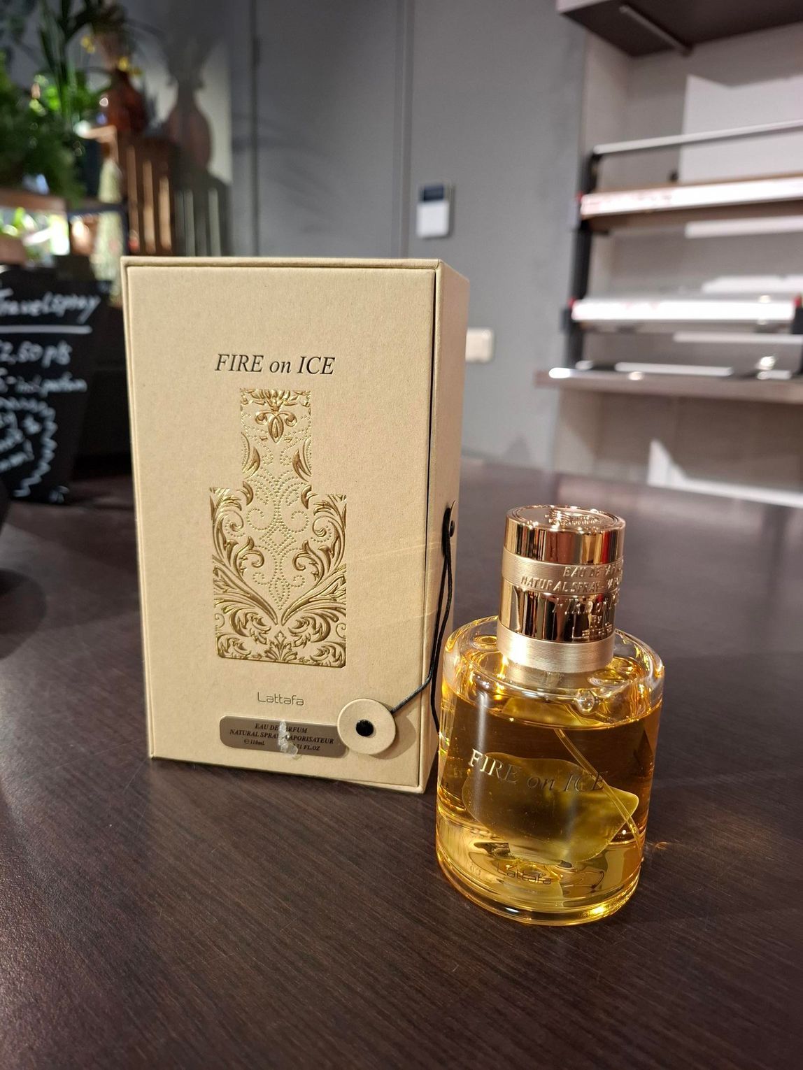 Een flesje parfum met goudkleurige vloeistof staat naast de beige, decoratieve doos op een donkerhouten ondergrond.