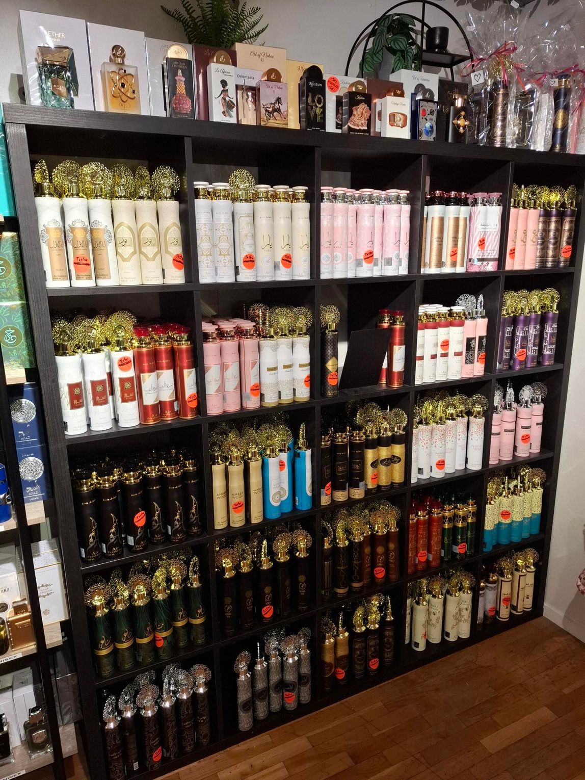 Een donkerhouten kast met meerdere vakken, gevuld met rijen verschillende flesjes parfum en sprays.