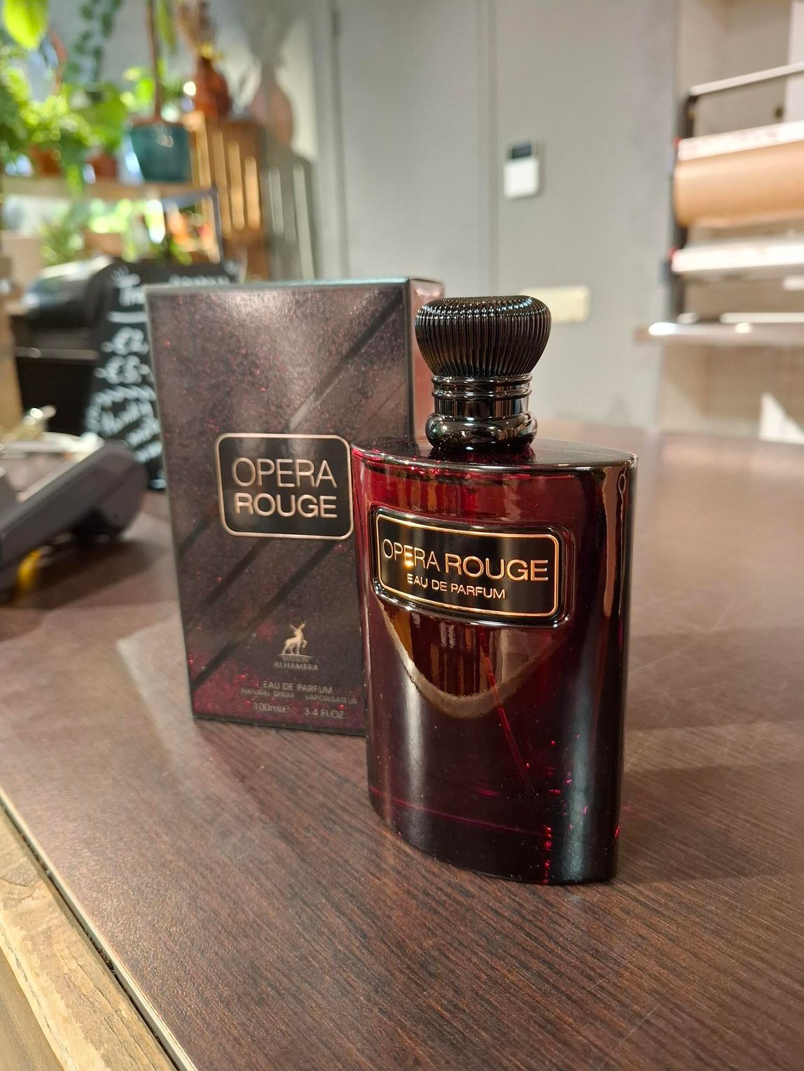 Een flesje parfum Opera Rouge staat naast de doos op een houten tafel.