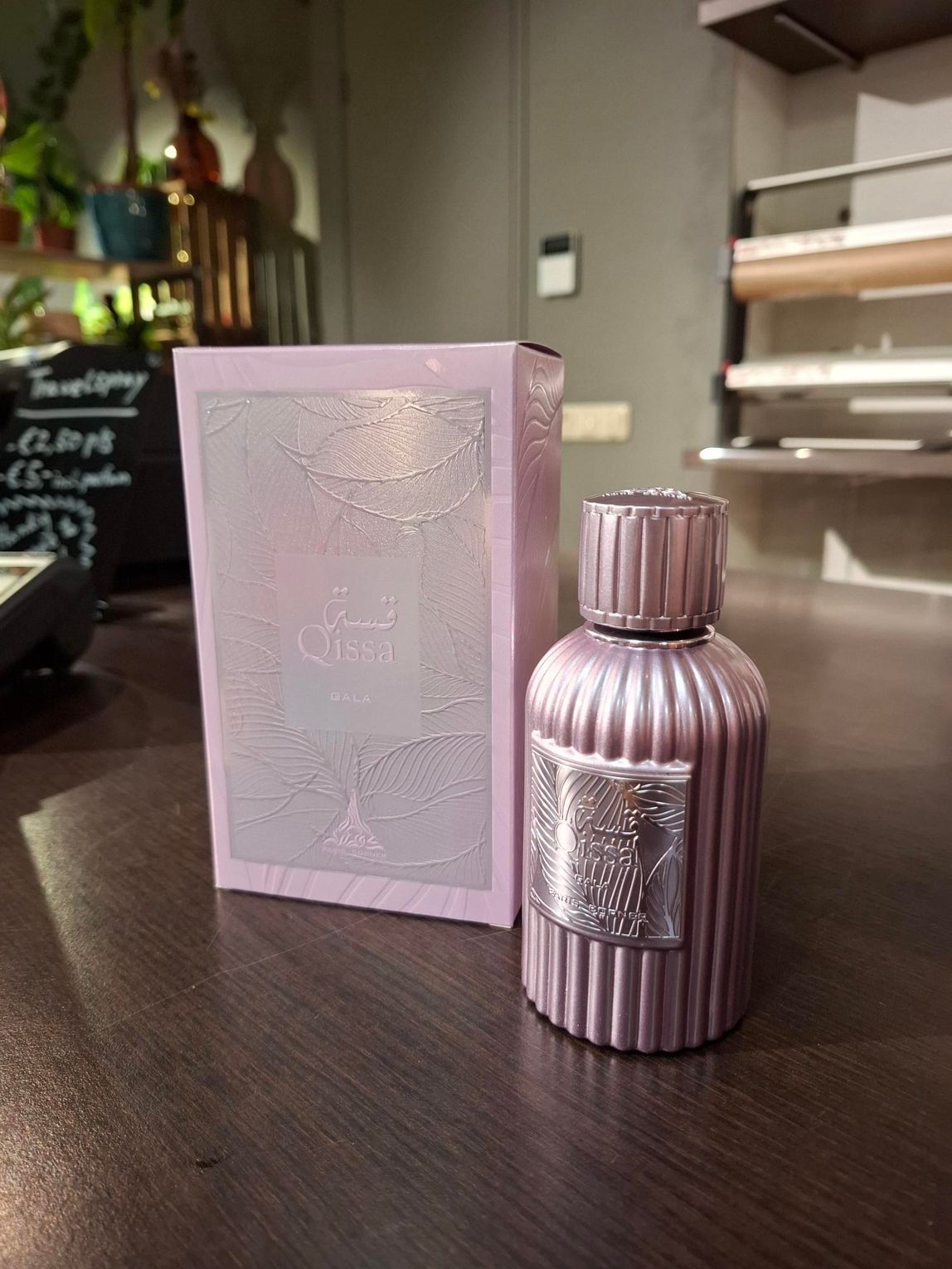 Een lichtpaarse parfumfles en de bijbehorende sierlijke doos staan ​​op een houten tafel in een binnenruimte.