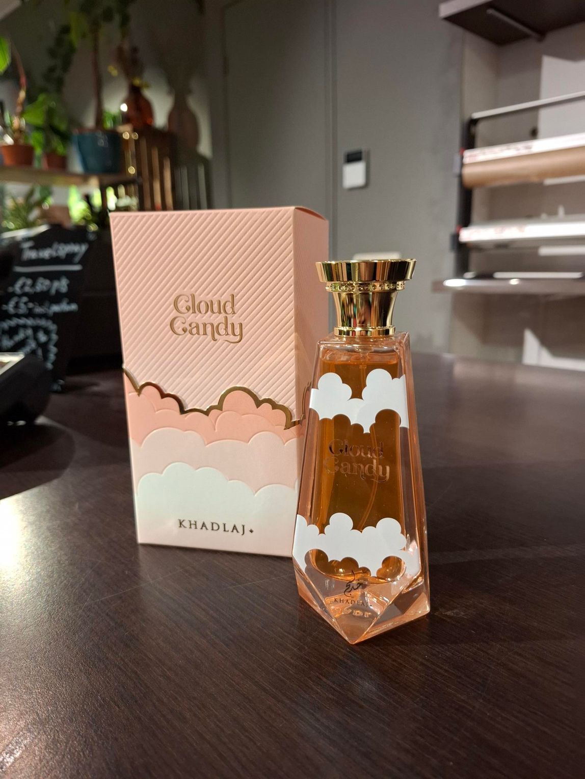 Een perzikkleurig flesje Cloud Candy-parfum en het bijbehorende doosje met een wit wolkje staan ​​op een donkerhouten ondergrond.