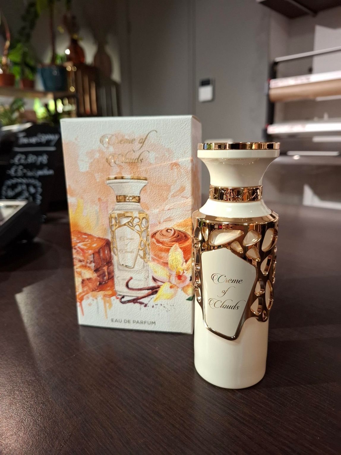 Een wit parfumflesje met gouden details staat naast de decoratieve doos met afbeeldingen van vanille en karamel.