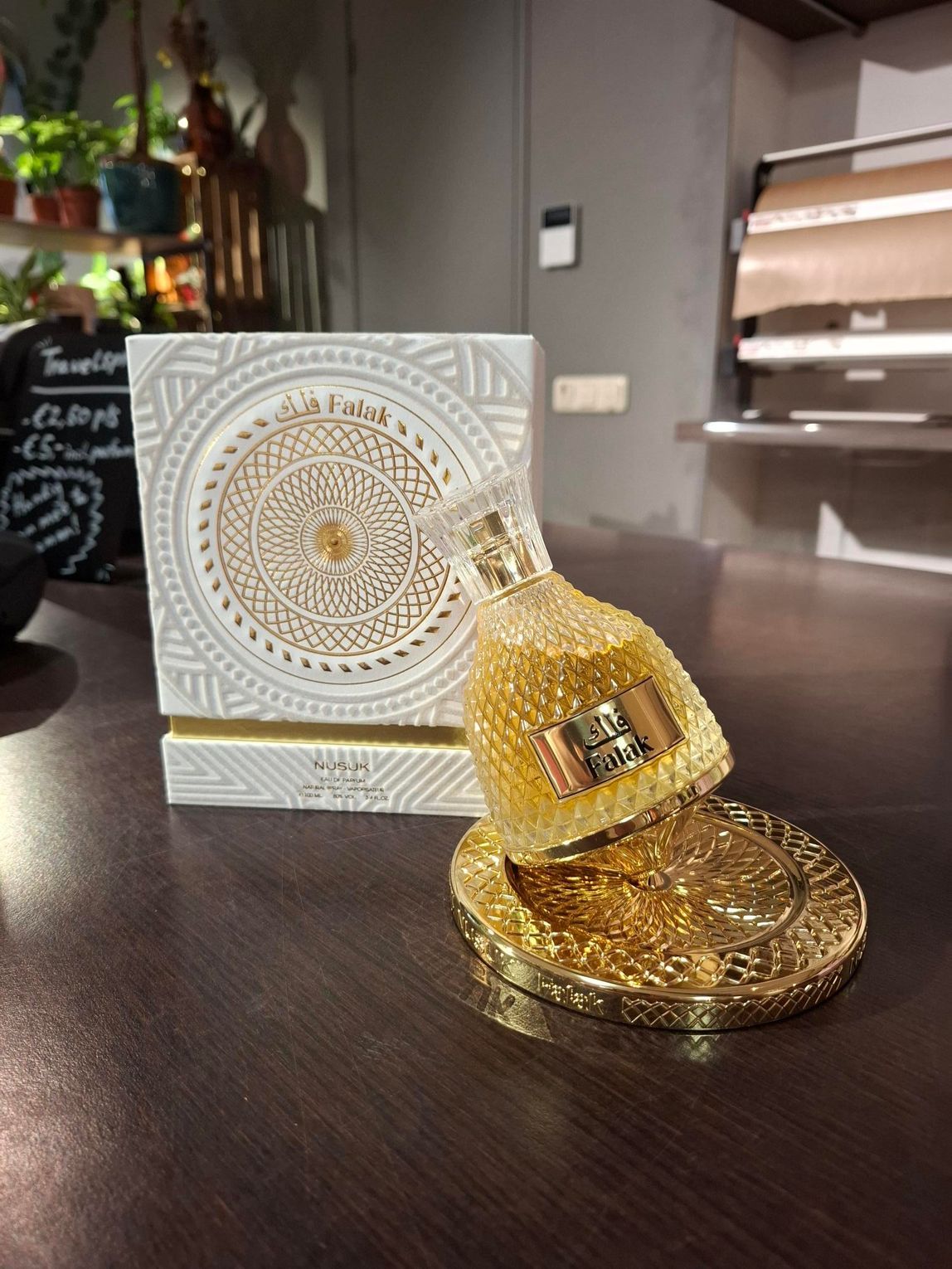 Een parfumflesje met gouden accenten en een gestructureerd oppervlak staat op een decoratieve gouden voet voor de bijpassende, witgedekte doos.