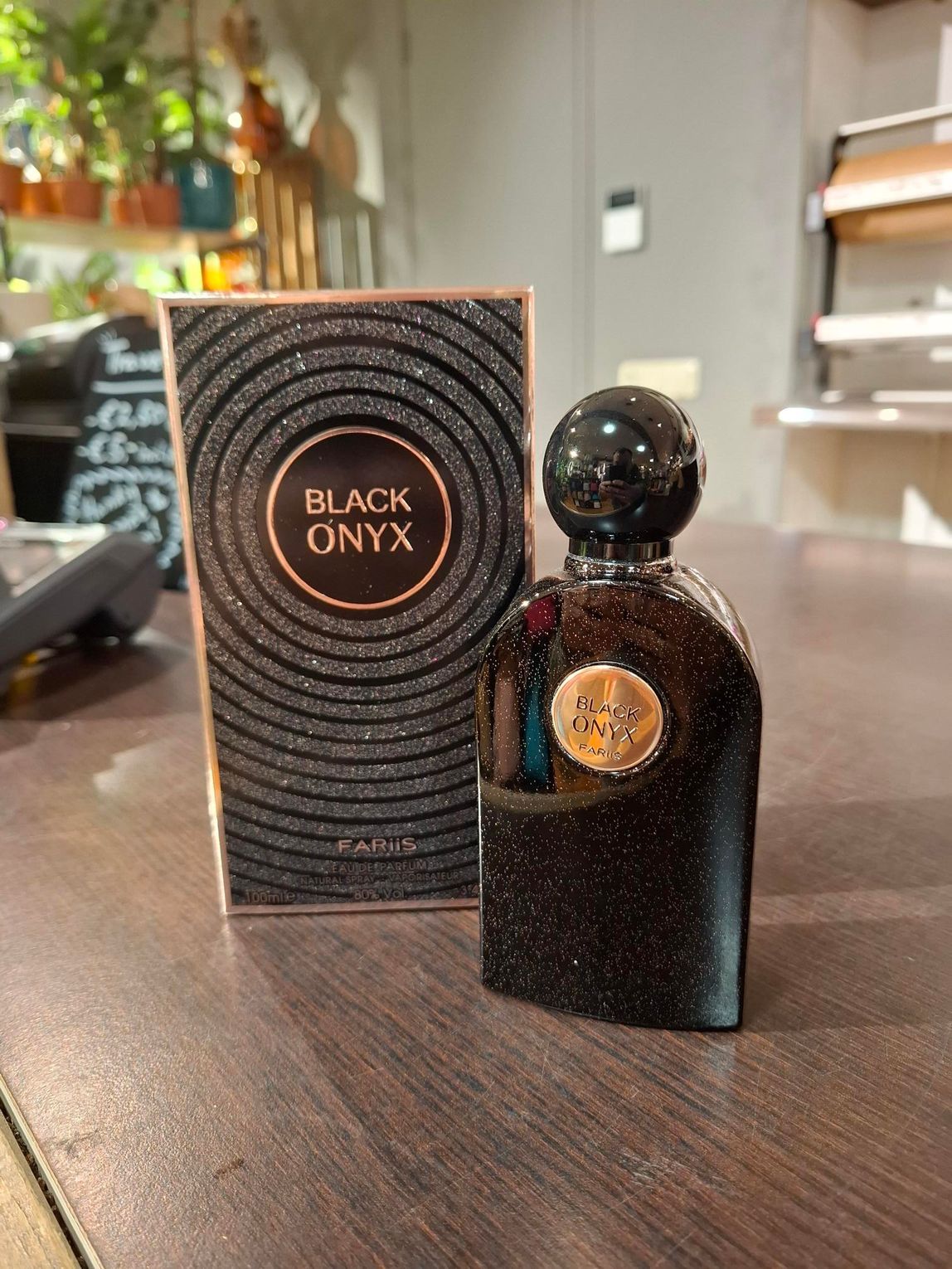 Het parfumflesje Black Onyx en de bijbehorende glinsterende zwarte doos met gouden letters staan ​​op een houten toonbank.