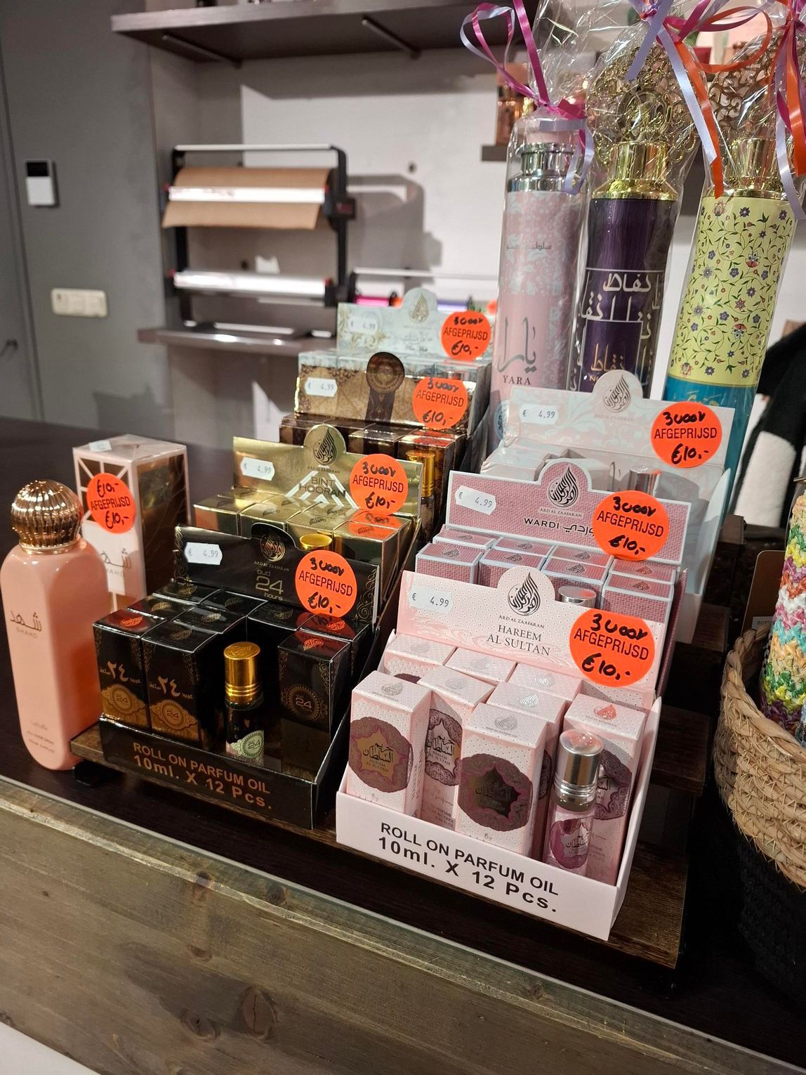 Een vitrine met diverse parfumflesjes en doosjes met parfum, voorzien van oranje prijskaartjes, op een houten toonbank.