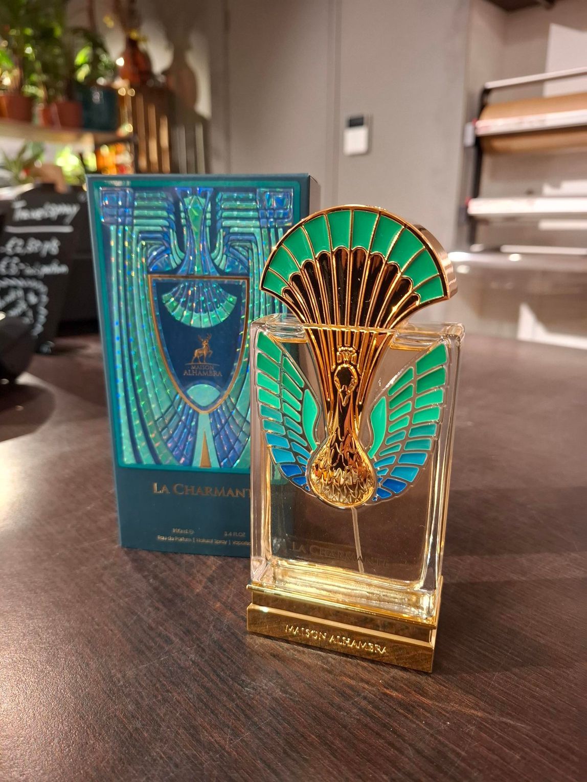 Een flesje Ra Chams-parfum met een sierlijk, op Egypte geïnspireerd, goud- en turkooizen embleem, naast de bijpassende turquoise doos.