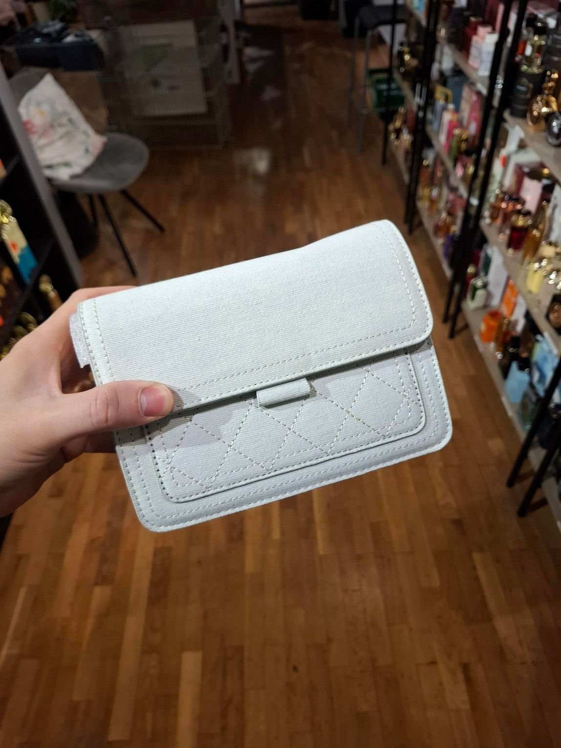 Hand die een witte, gestructureerde clutch vasthoudt in een winkelgang.