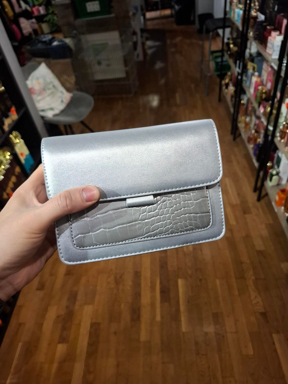 Hand die een zilveren portemonnee vasthoudt in een winkelgang met schappen op de achtergrond.