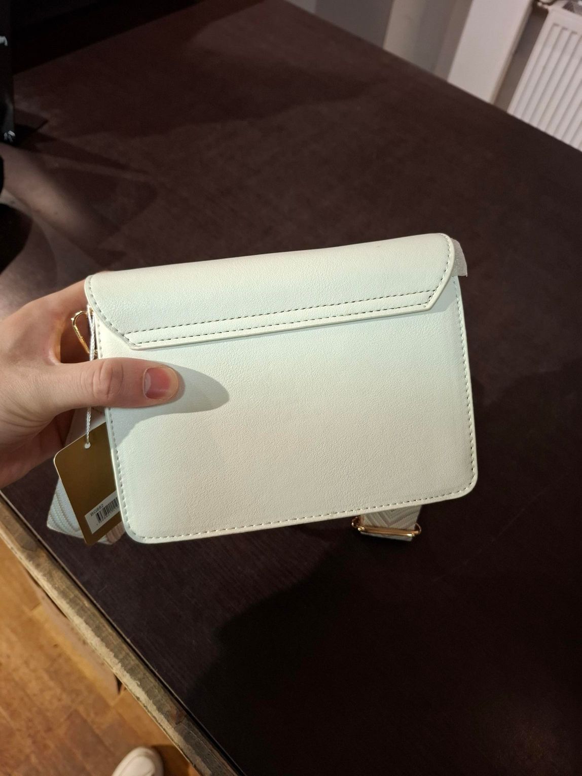 Hand die een blauwe portemonnee met patroon vasthoudt boven een houten vloer in een winkel of interieur van een woning.