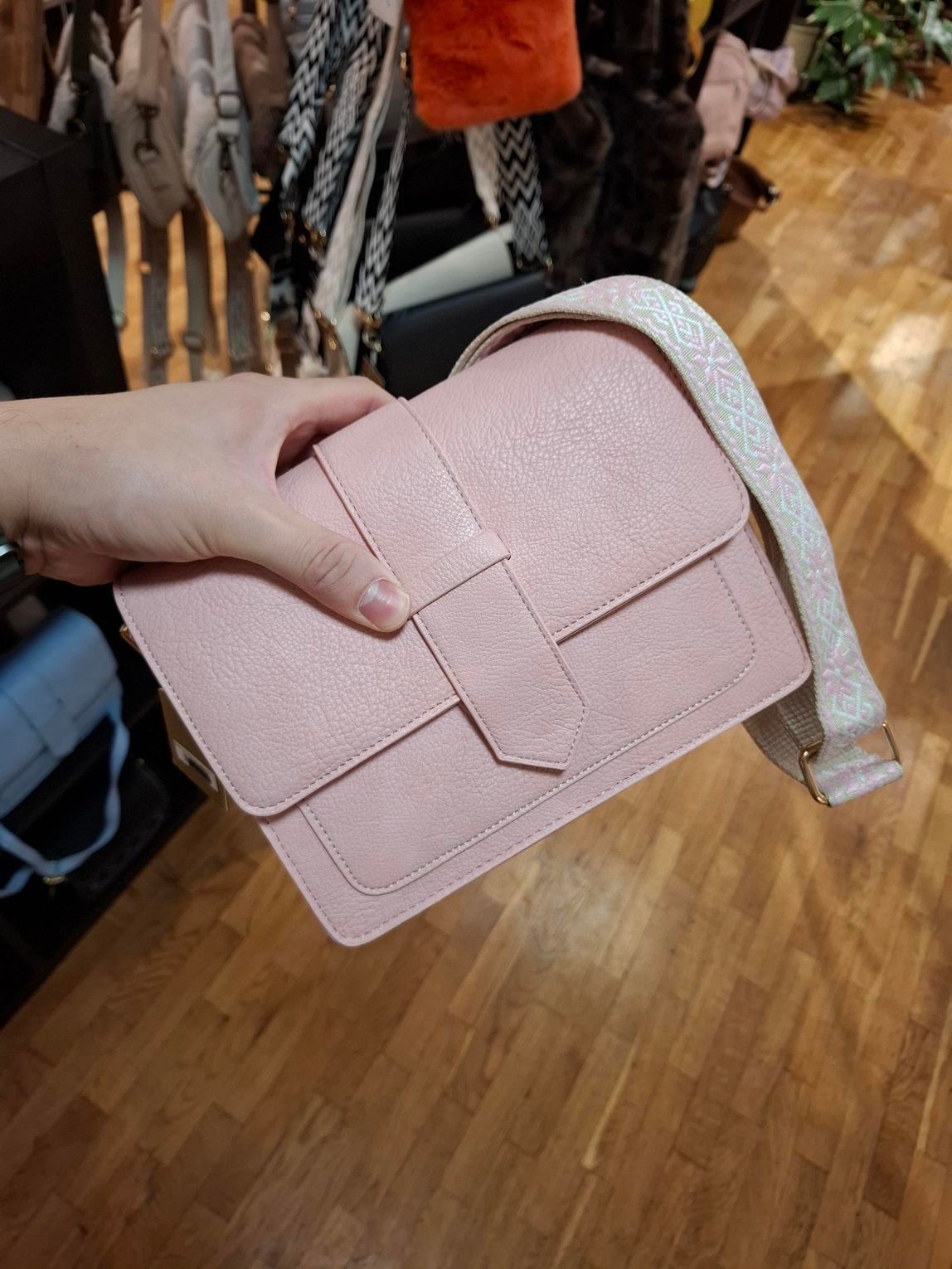 Hand die een roze gewatteerde handtas met een witte schouderband vasthoudt in een winkel.