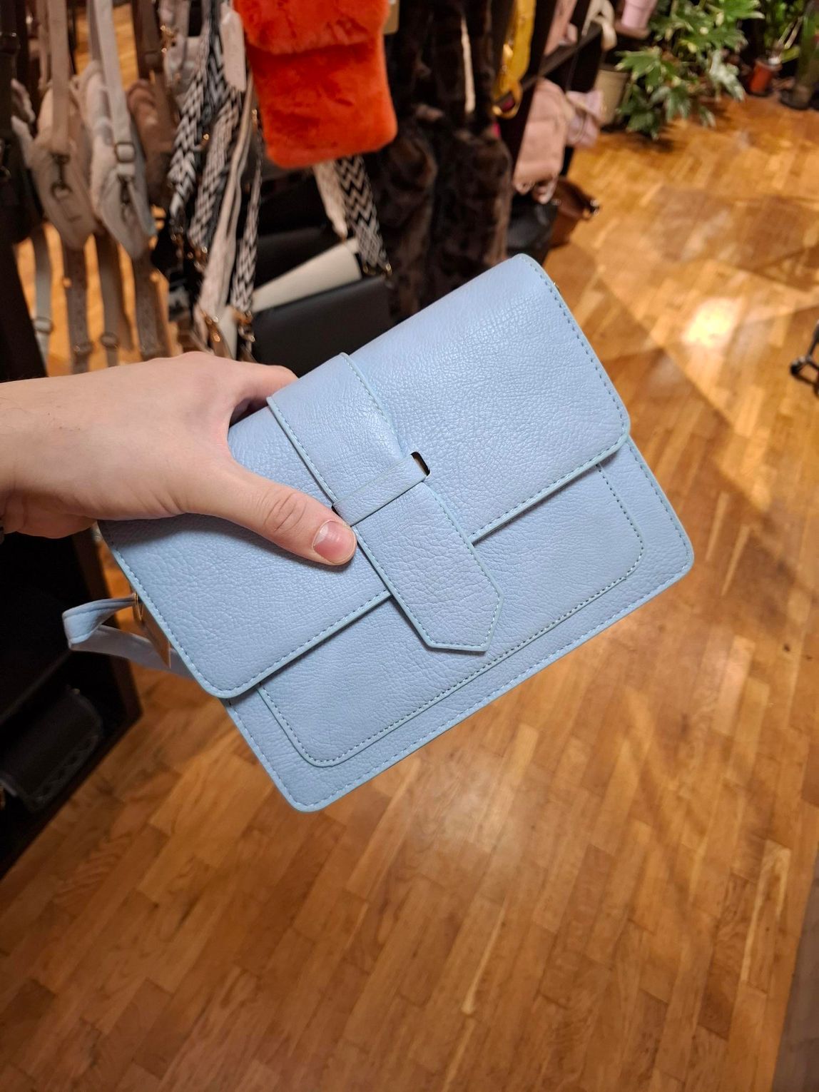 Hand die een lichtblauwe, gestructureerde clutch vasthoudt in een kledingwinkel.