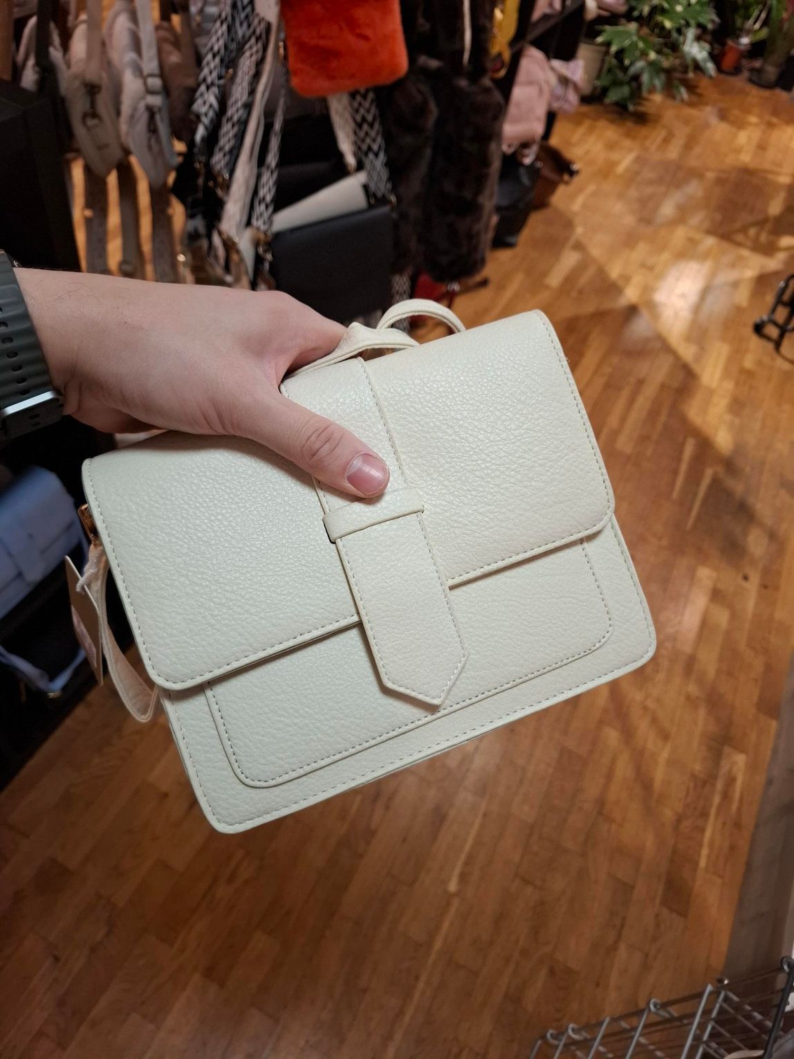 Hand die een crèmekleurige, gewatteerde handtas vasthoudt in een kledingwinkel.