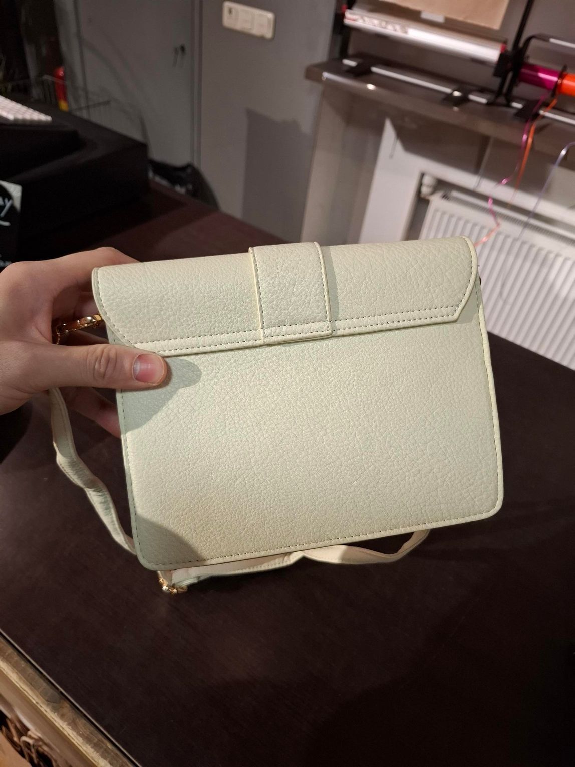 Hand die een roze gewatteerde handtas met een witte schouderband vasthoudt in een winkel.
