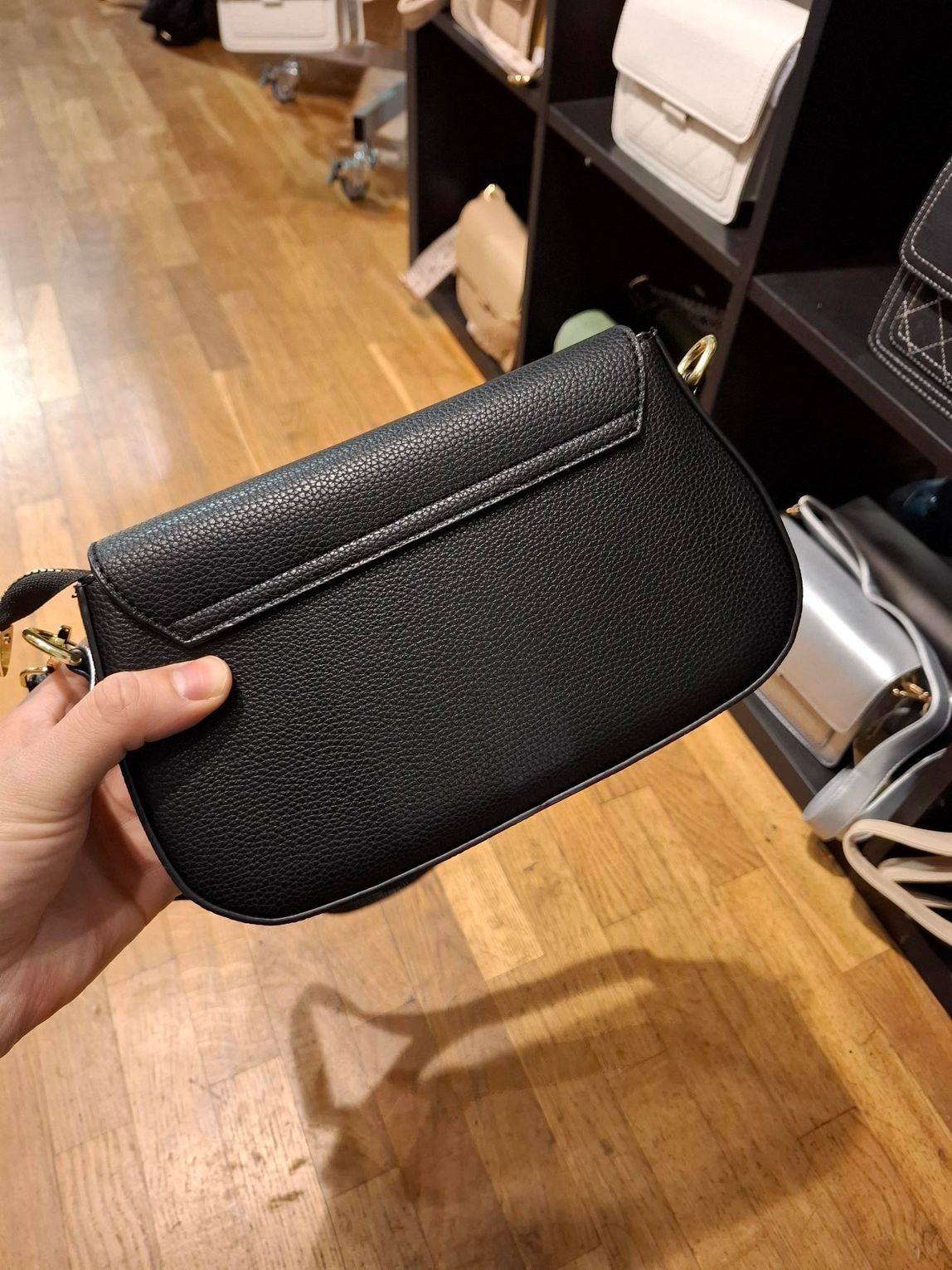 Hand die een klein zwart, gestructureerd handtasje met gouden sluiting vasthoudt in een boetiek.