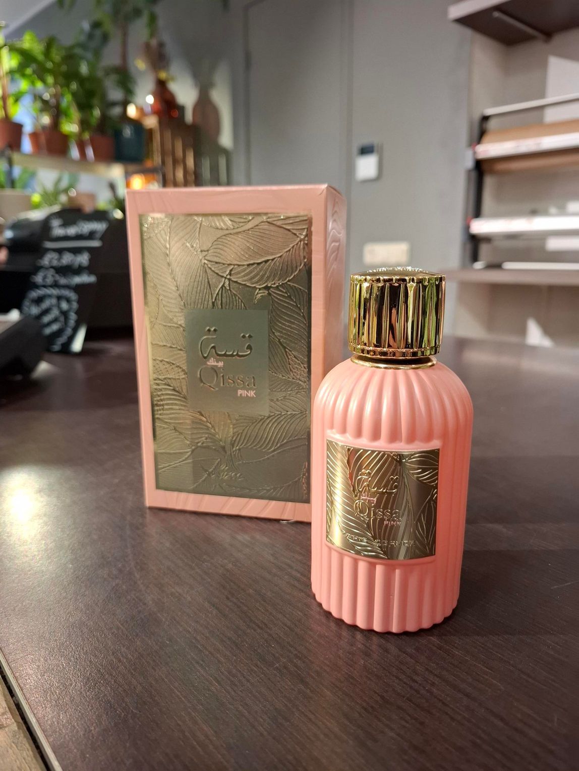 Een perzikkleurig parfumflesje met een gouden dop en etiket staat naast het bijpassende doosje op een donkere ondergrond.