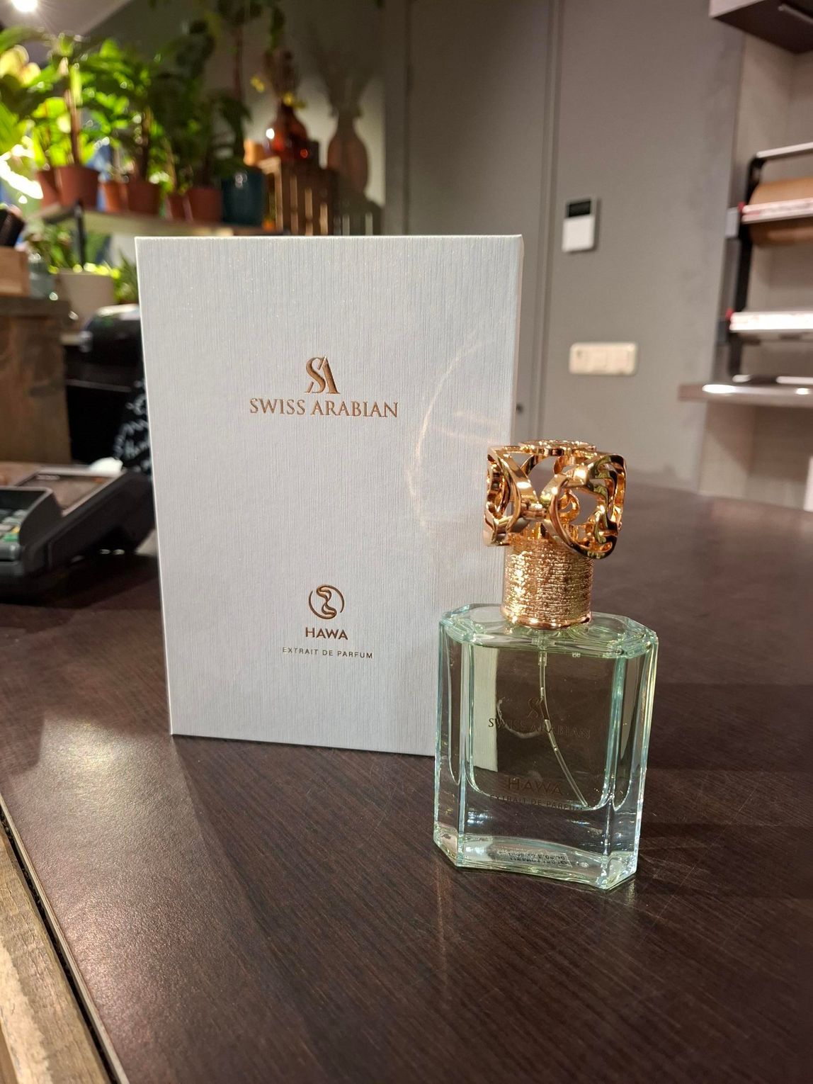 Een flesje parfum Paris Arabian met de bijbehorende witte doos, staand op een donkerhouten tafel in een binnenruimte.