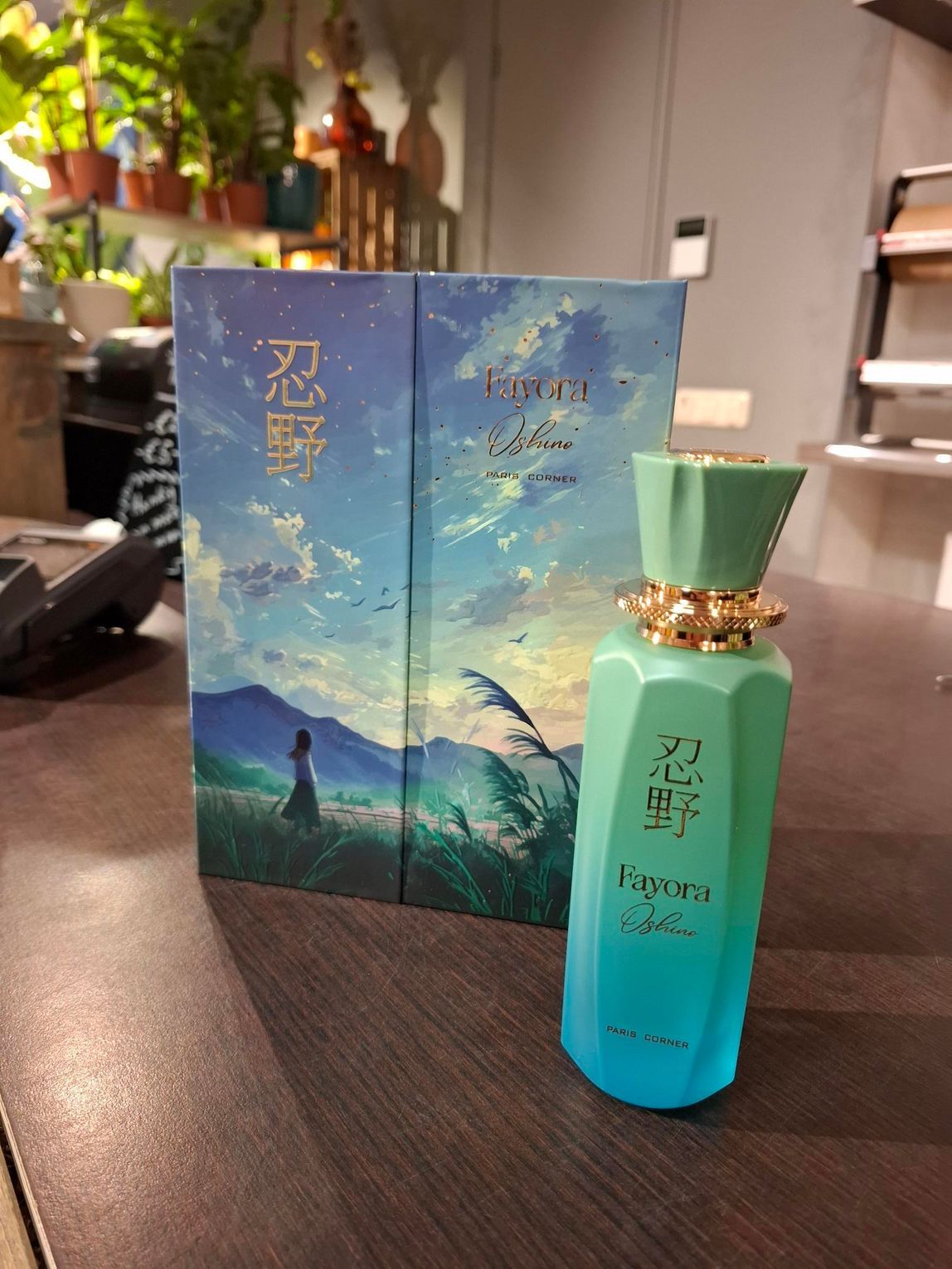 Een blauwgroene parfumfles en het bijbehorende doosje, beide met landschapsillustraties en Aziatische tekst, op een bureau.