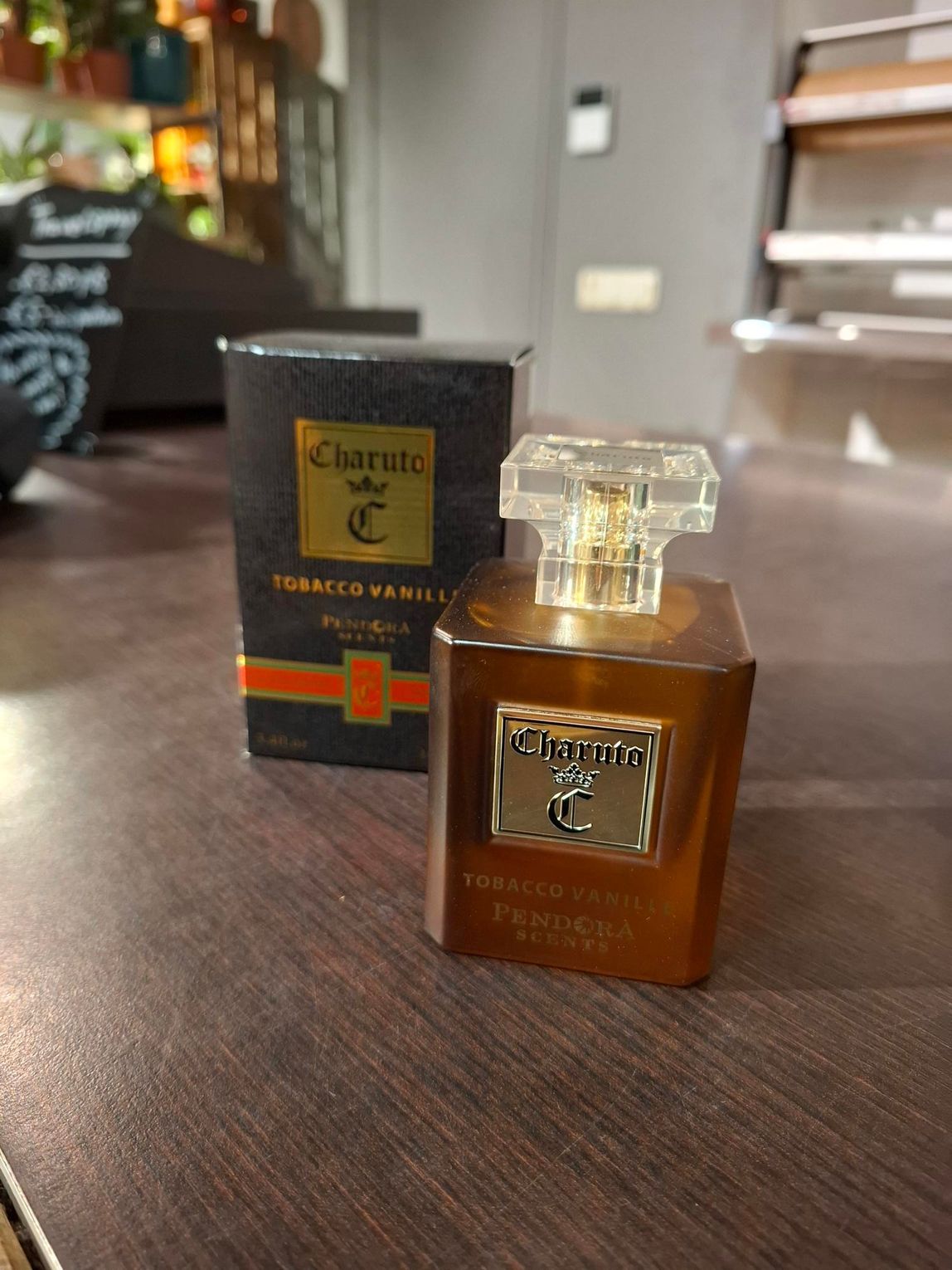 Een flesje parfum Charuto Tobacco Vanille staat naast de zwart-gouden productverpakking op een houten ondergrond.