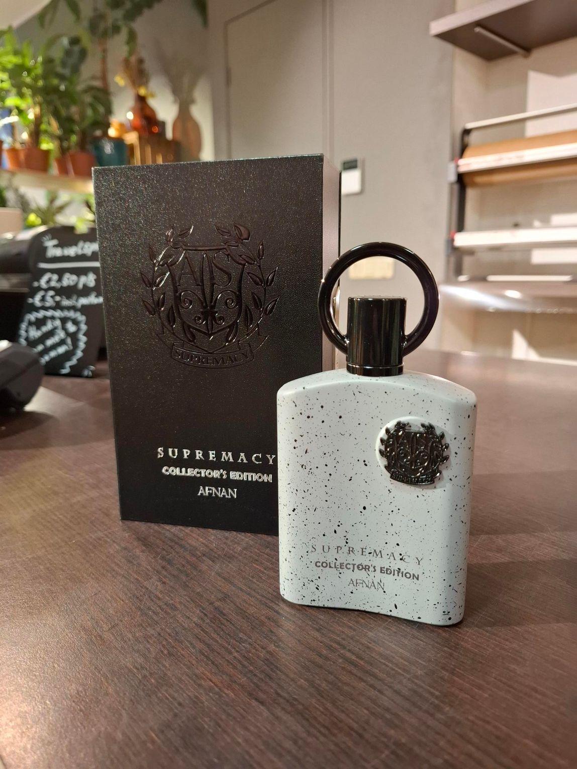 Een flesje Afnan Supremacy Incense parfum en de bijbehorende zwarte, gestructureerde doos staan ​​op een houten tafel in een winkelomgeving.