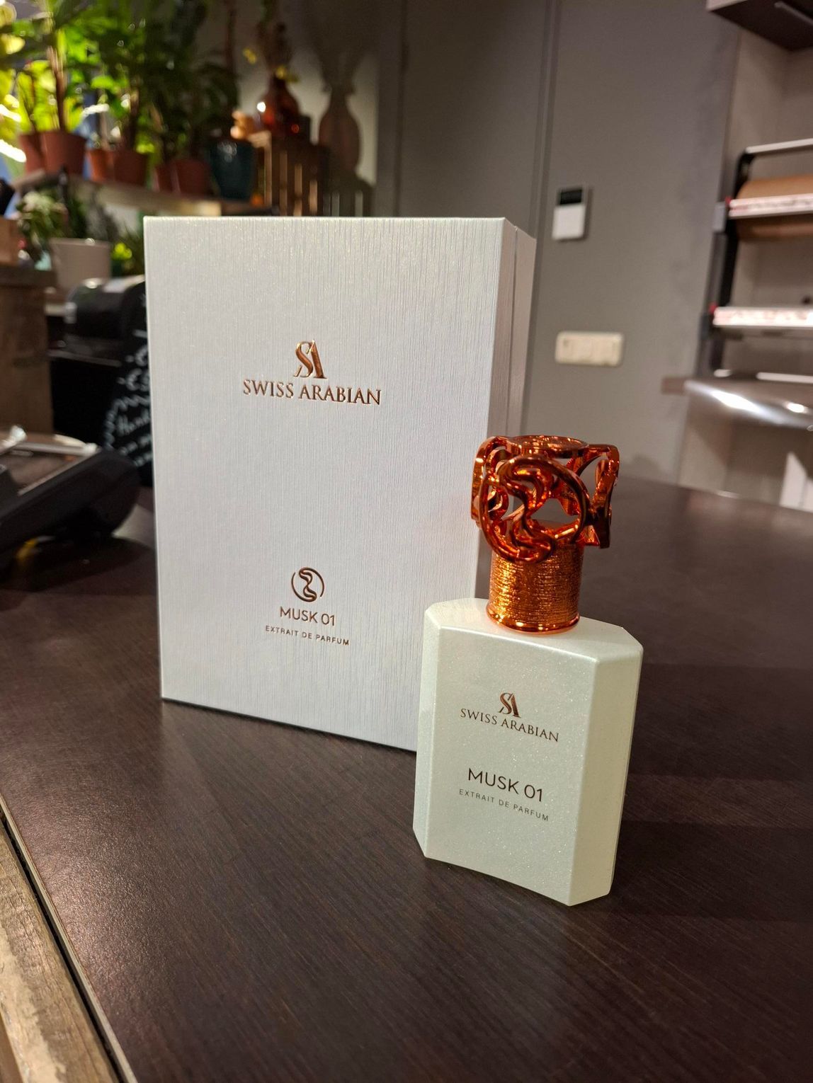 Een flesje Swiss Arabian Musk 07 parfum met een sierlijke koperen dop staat naast de witte doos op een houten tafel.