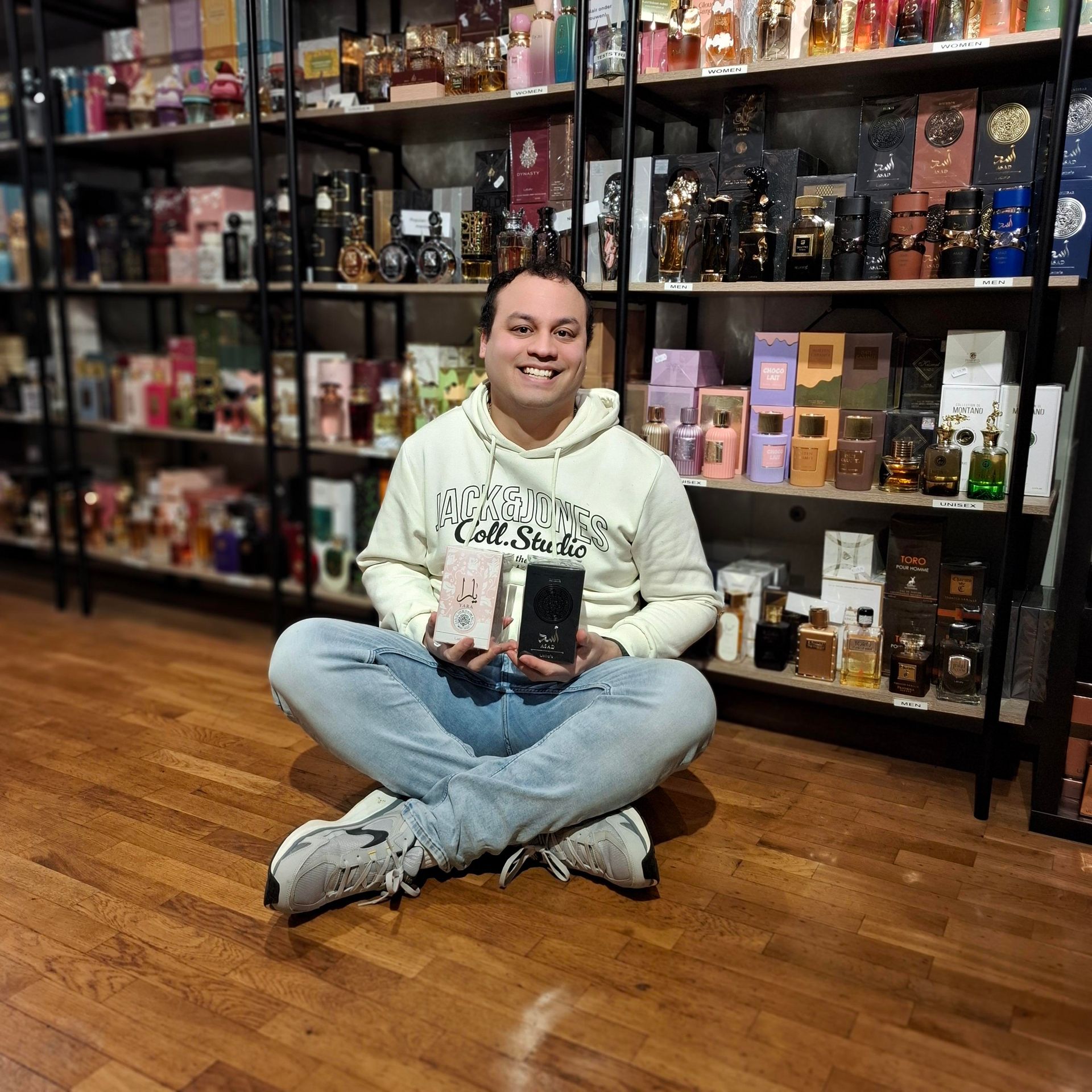 Een persoon met kort haar en een bril glimlacht terwijl hij zijn gezicht in zijn handen laat rusten, zittend aan een bureau met een laptop.