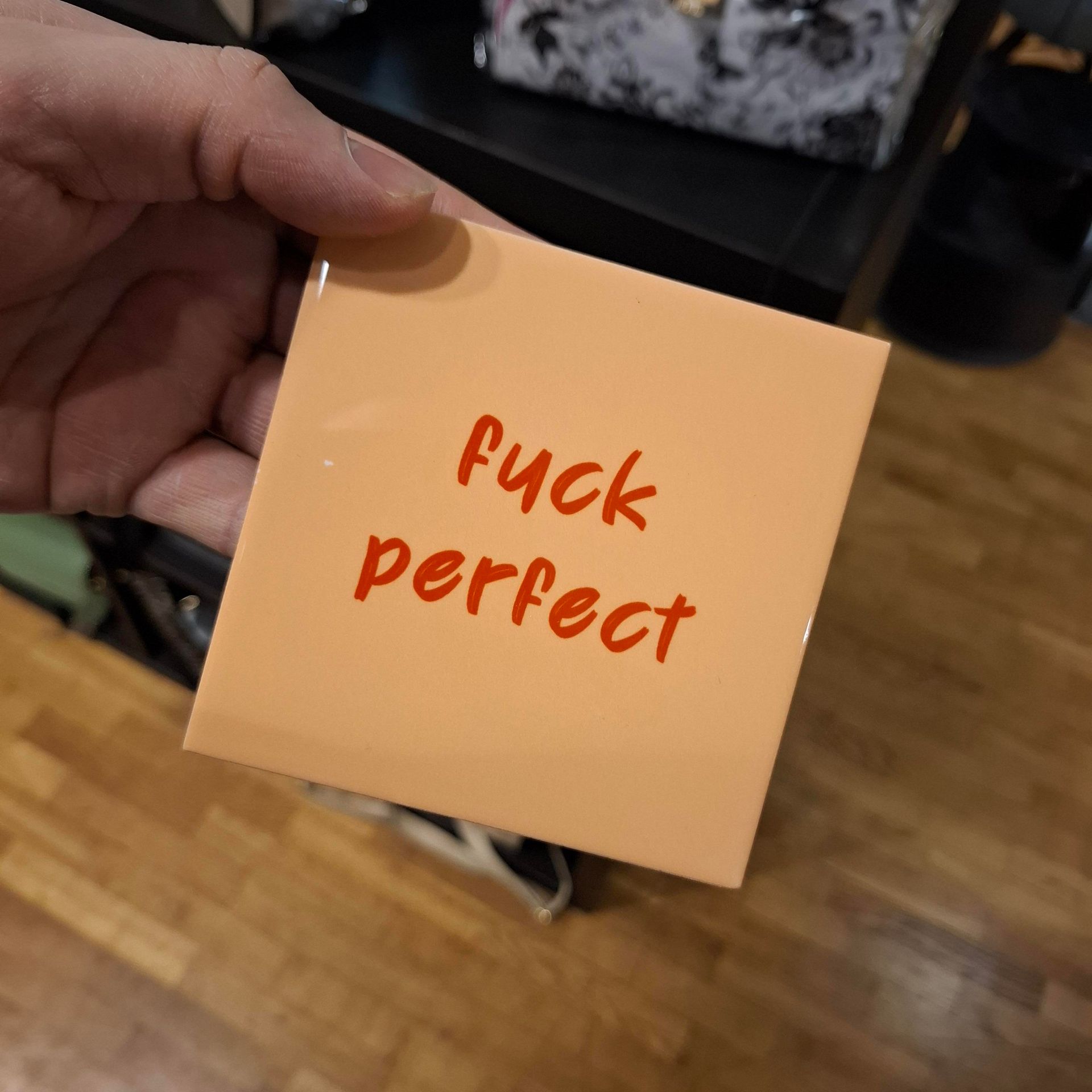 Hand die een perzikkleurig plakbriefje vasthoudt met rode, handgeschreven tekst waarop staat: 