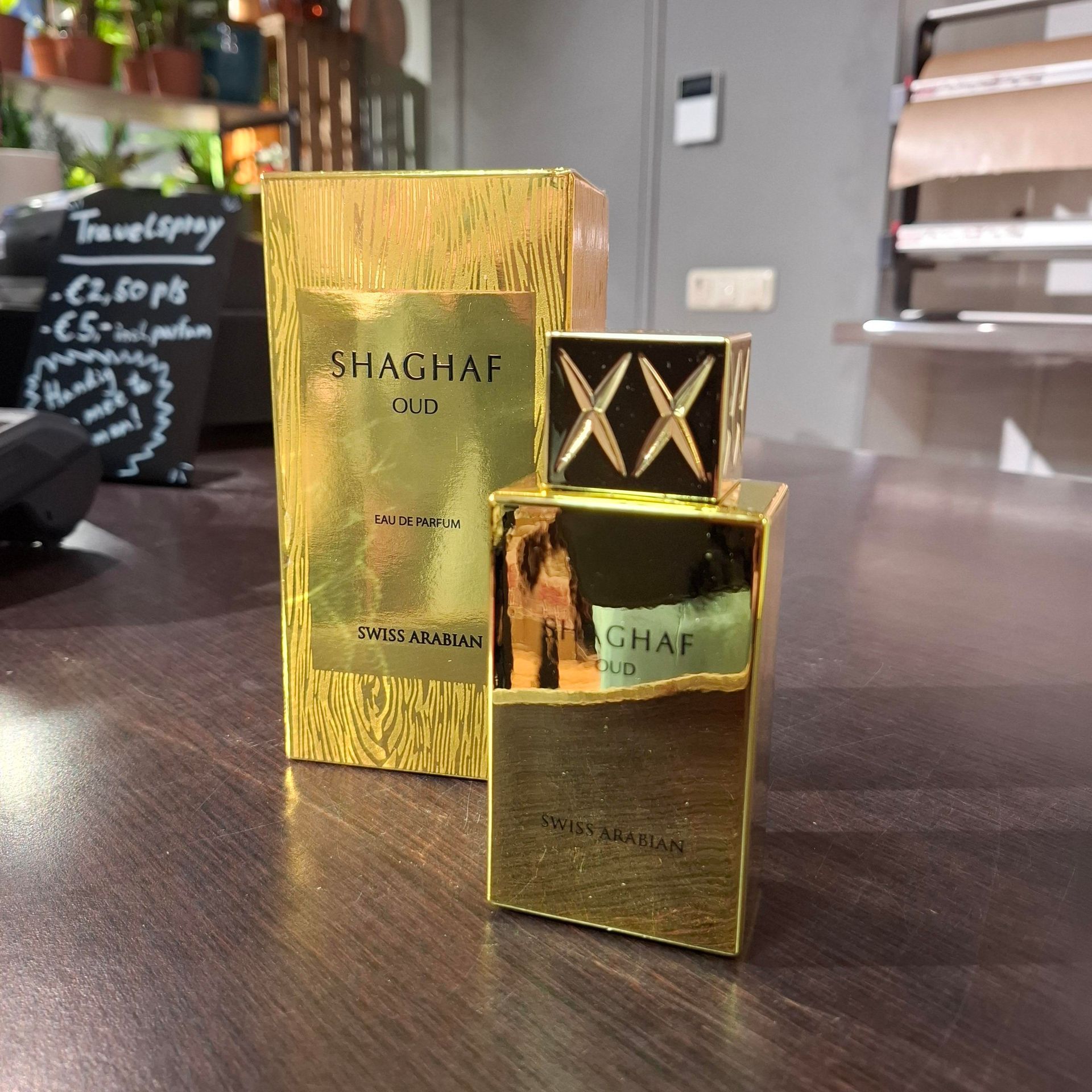 Een gouden fles Swiss Arabian Shaghaf Oud parfum met bijbehorende gouden doos, staand op een donkerhouten ondergrond.