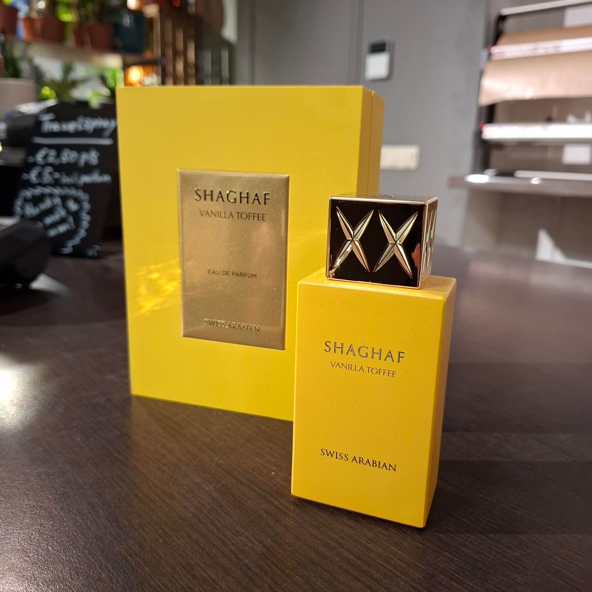 Een felgele parfumfles en het bijbehorende rechthoekige doosje staan ​​op een donkere ondergrond in een winkelomgeving.