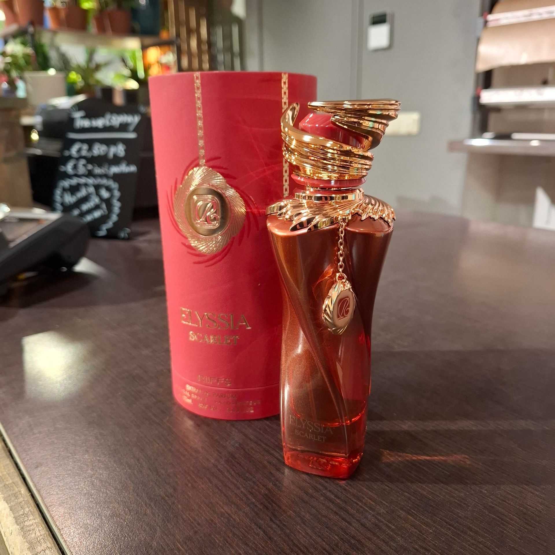 Een bronzen parfumflesje met een gouden slangendop en hanger, naast de bijpassende cilindrische rode doos.