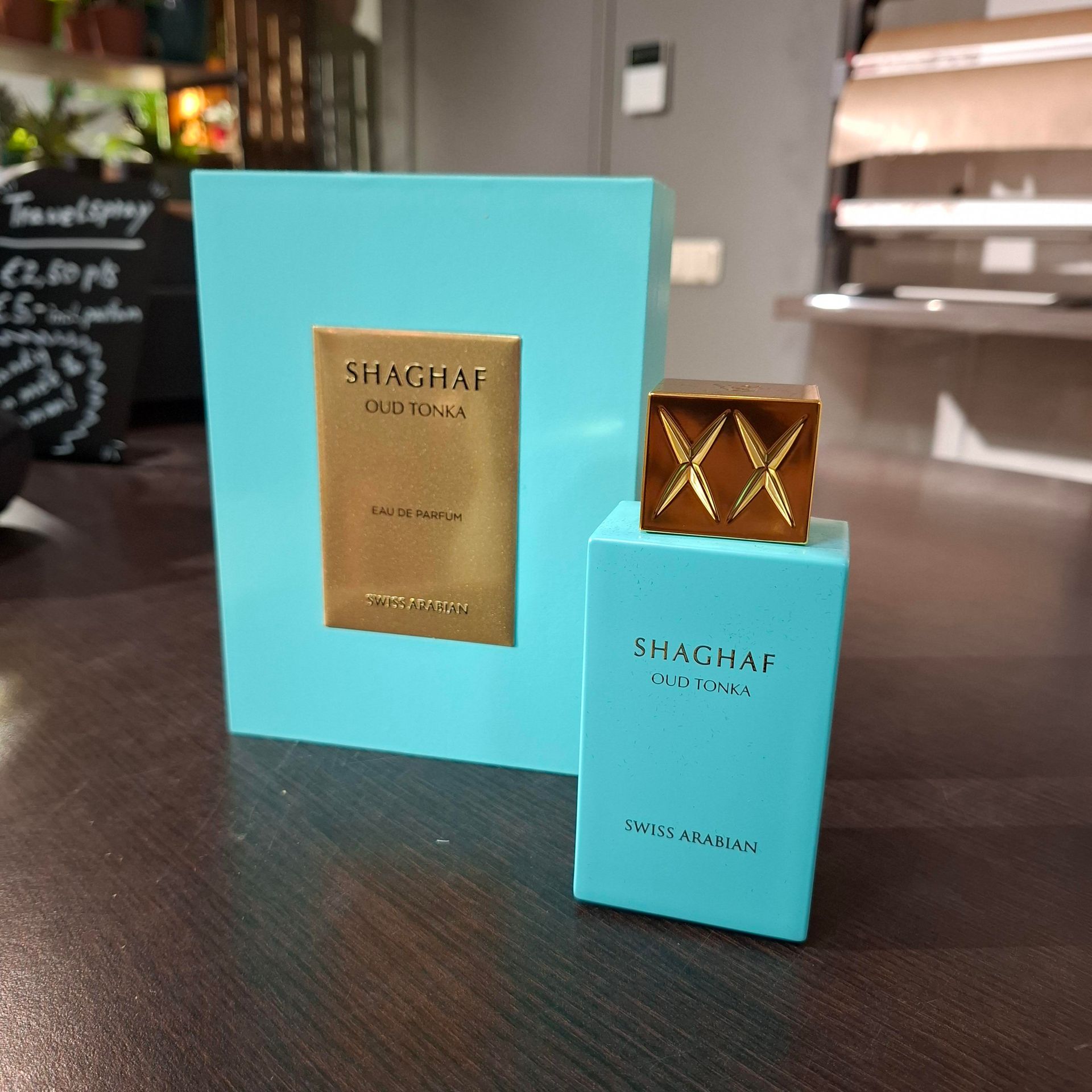 Een fles en bijpassende doos Shaghaf Oud Tonka parfum, met een levendige turquoise verpakking en gouden accenten.