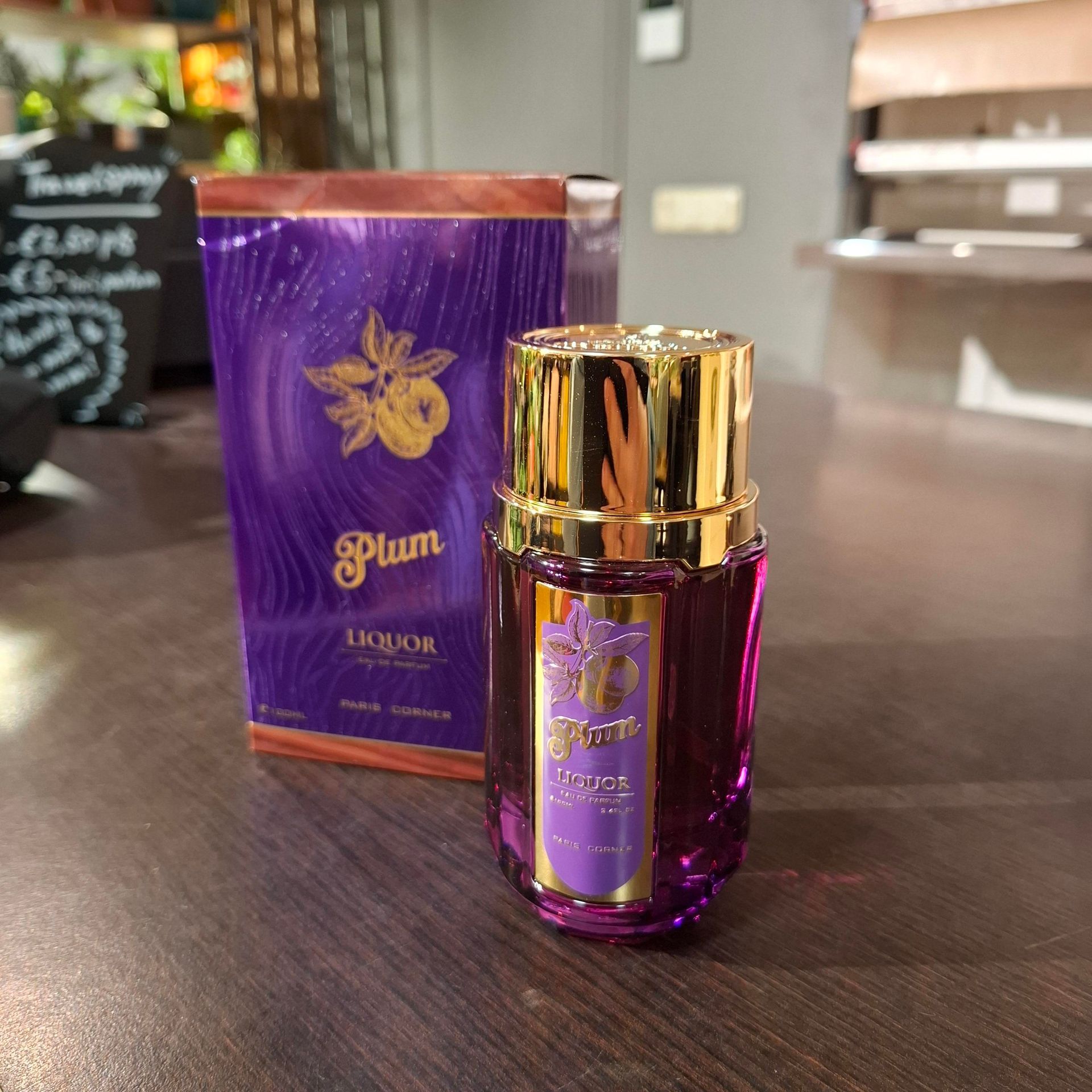Een paarse fles Plum Liquor-parfum met bijbehorende doos, tentoongesteld op een houten ondergrond.