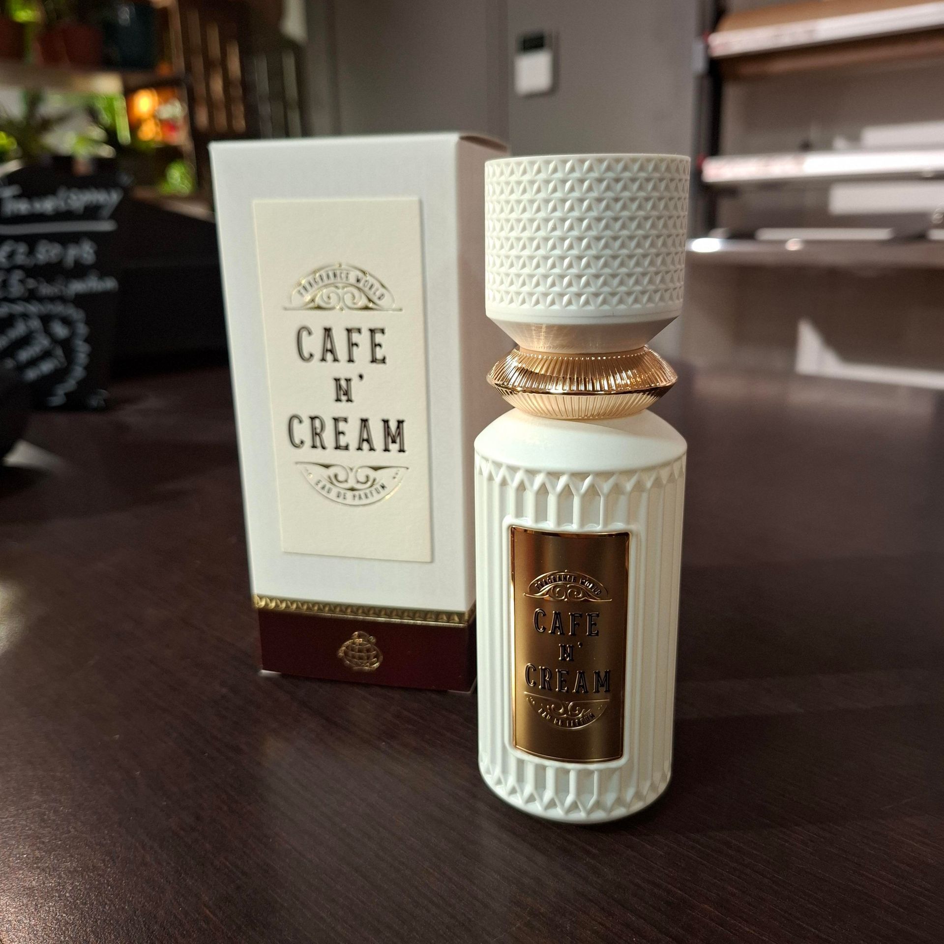 Een flesje Cafe N' Cream parfum met de bijbehorende witte doos staat op een donkerhouten ondergrond.