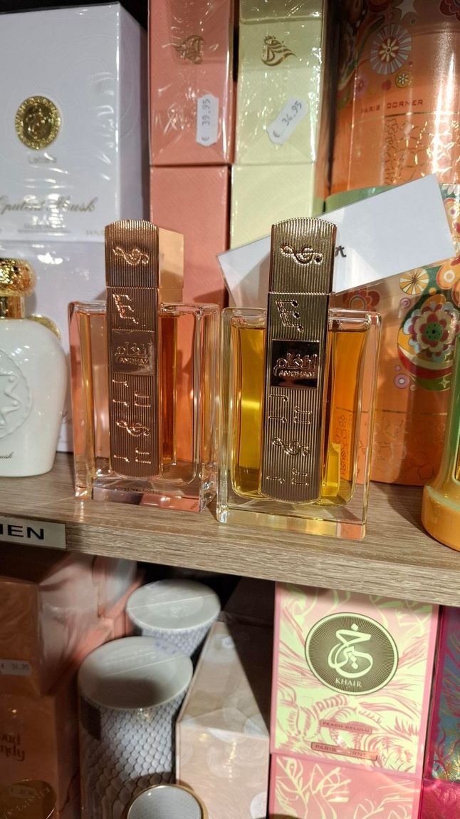 Op de planken staan ​​diverse parfums in doosjes en flesjes uitgestald, waaronder twee opvallende glazen flessen met gouden decoratieve etiketten.