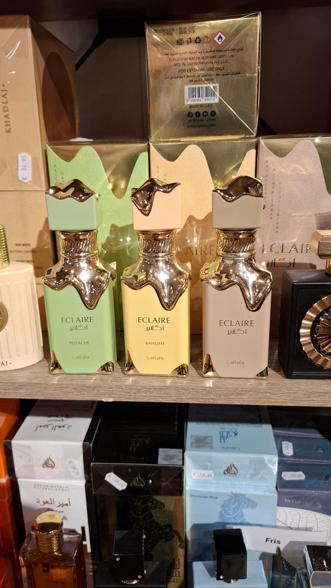 Een winkelschap met drie bij elkaar passende parfumflesjes in lichtgroen, geel en beige, met daaronder diverse doosjes.