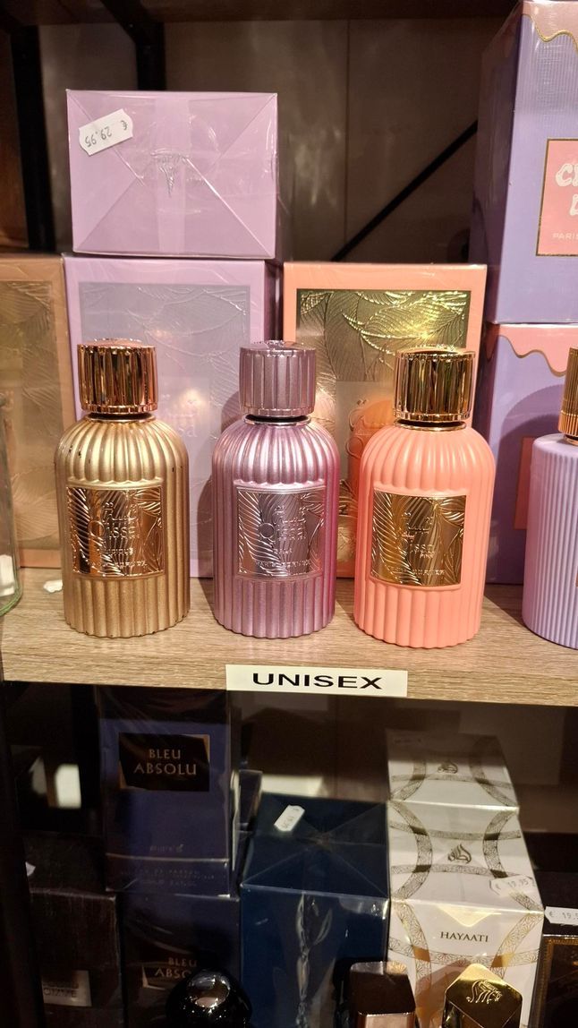 Drie decoratieve glazen parfumflesjes in goud, paars en perzik staan ​​op een winkelplank voor hun verpakkingen.