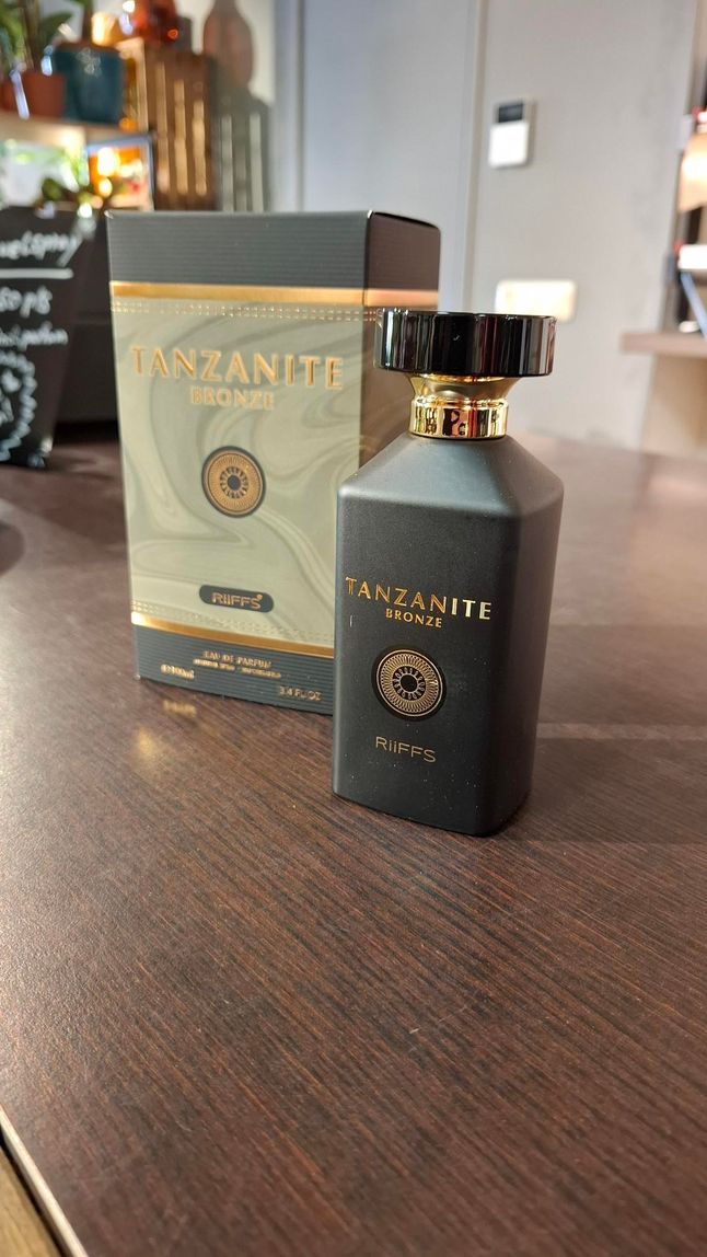 Zwarte parfumfles met gouden dop naast het bijpassende doosje op een houten tafel.