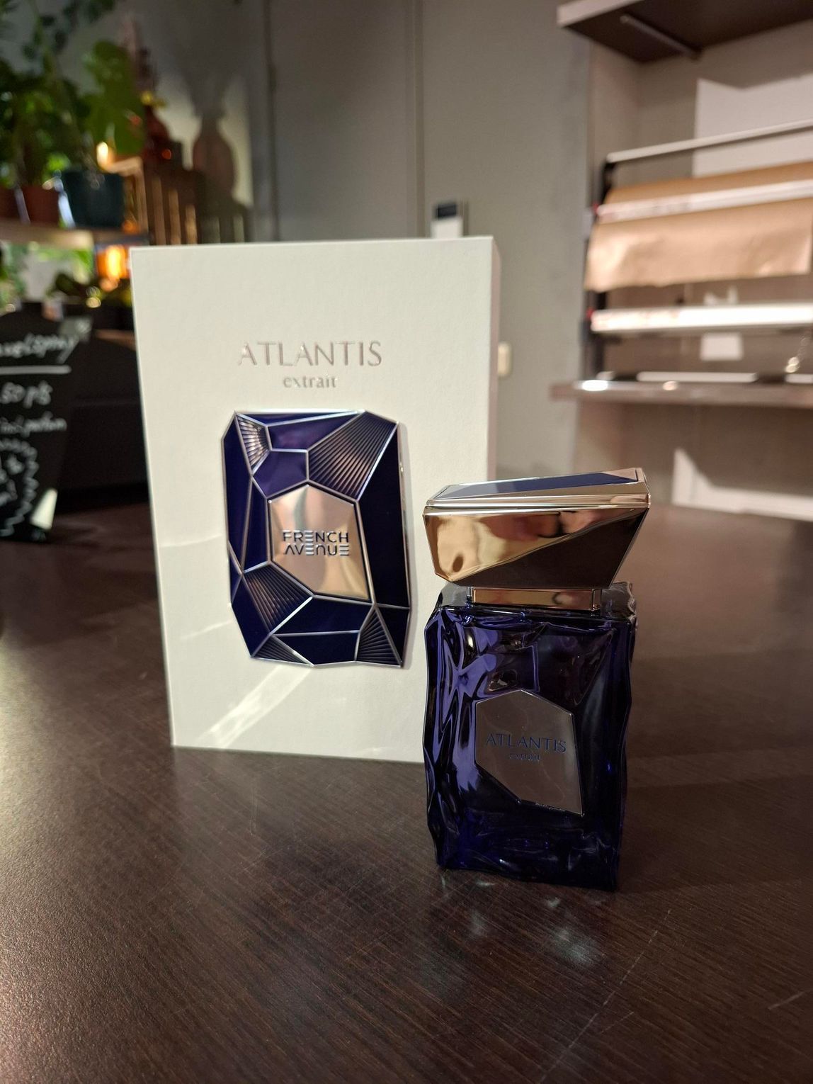 Een flesje Atlantis-parfum met een gestructureerde, diepblauwe glazen voet en een gouden dop, naast de bijpassende doos.