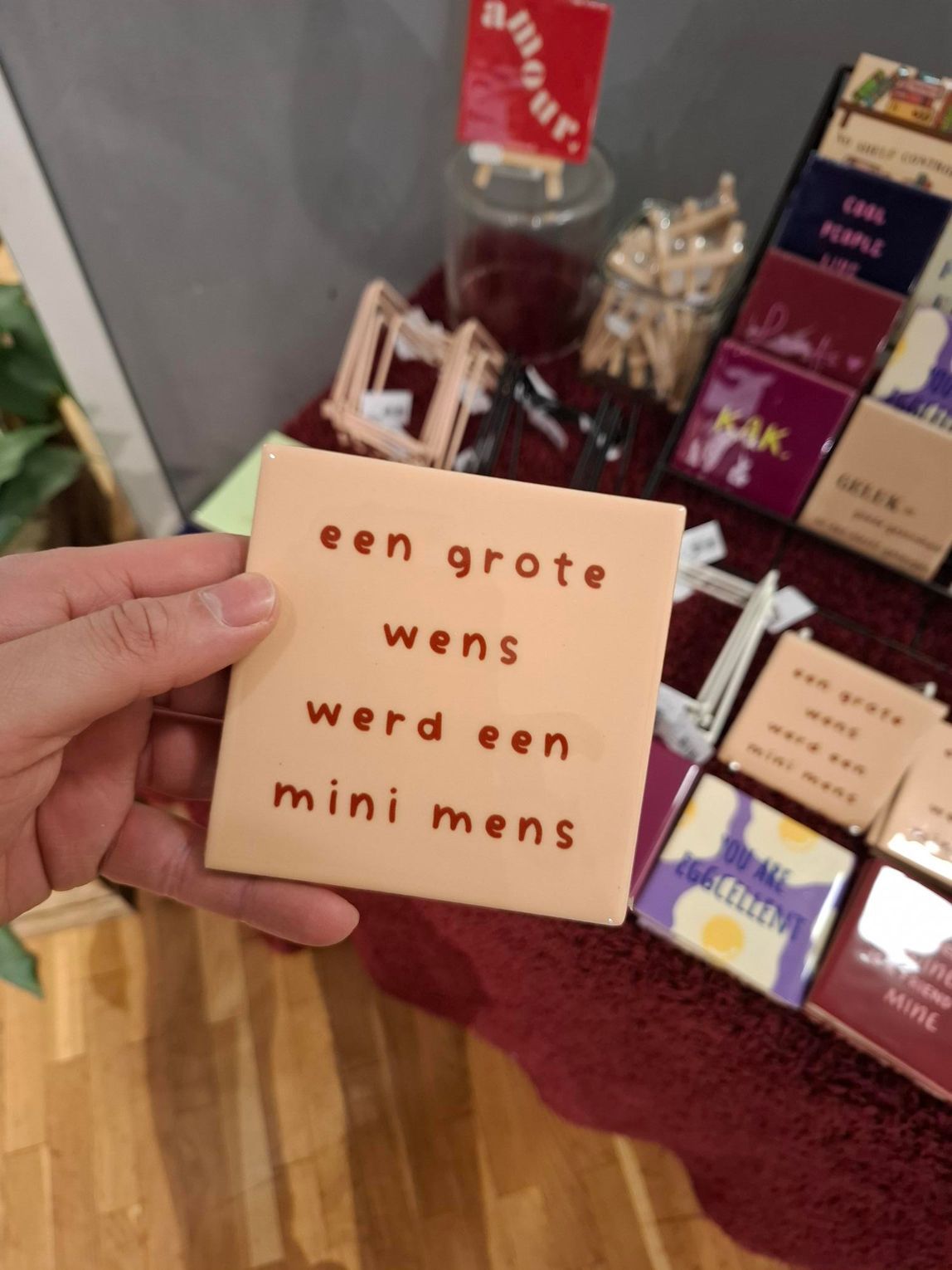 Een hand houdt een roze briefje met Nederlandse tekst vast, naast een display met chocolaatjes en geschenkdozen.