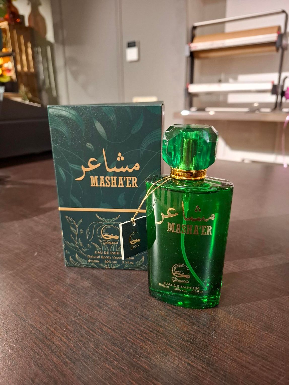 Groene parfumfles en bijpassende doos met gouden Arabische letters op een houten tafel.