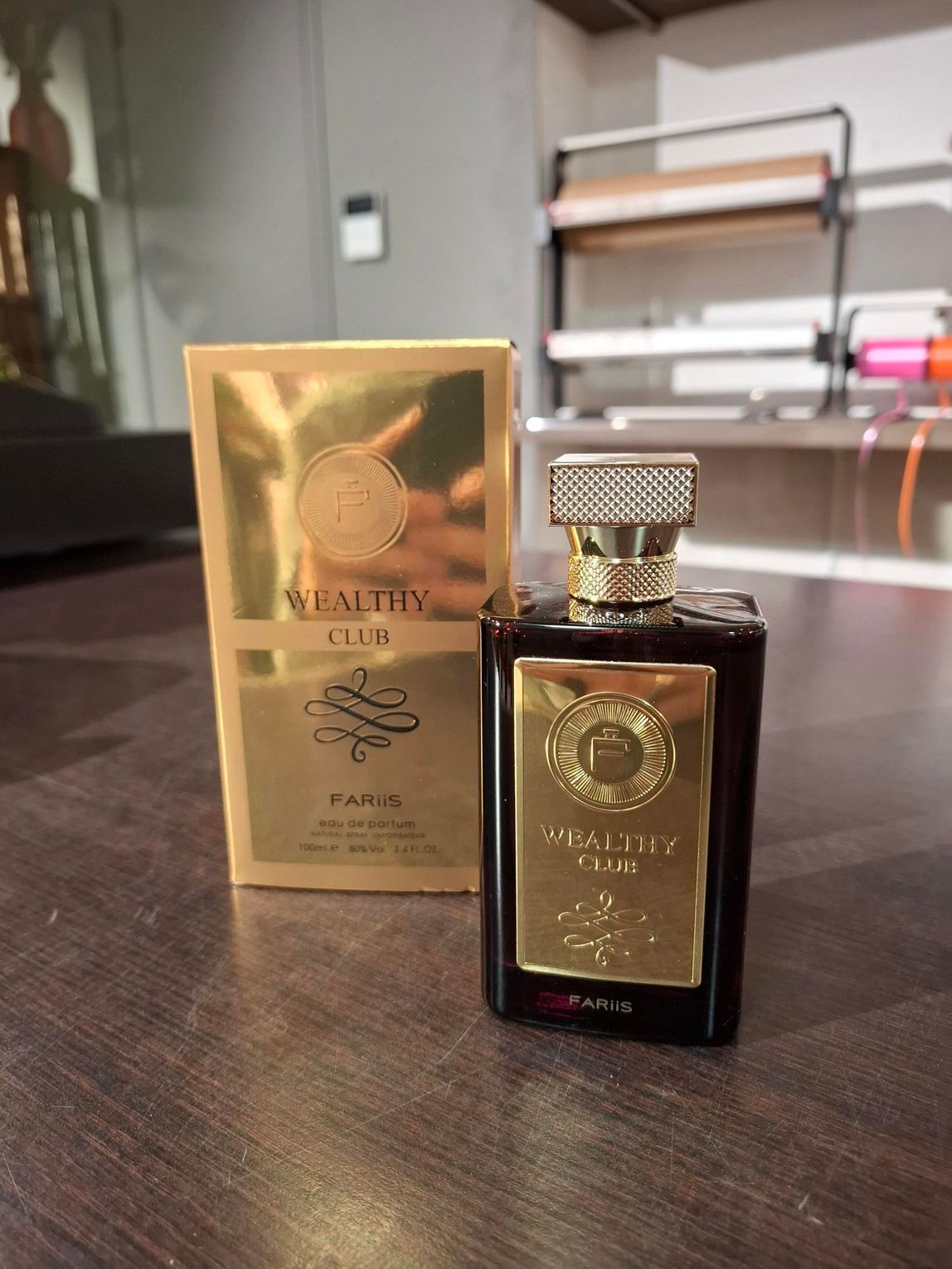 Twee donkere parfumflesjes met gouden etiketten staan ​​op een tafel, waarvan er één in een gouden doosje erachter staat.