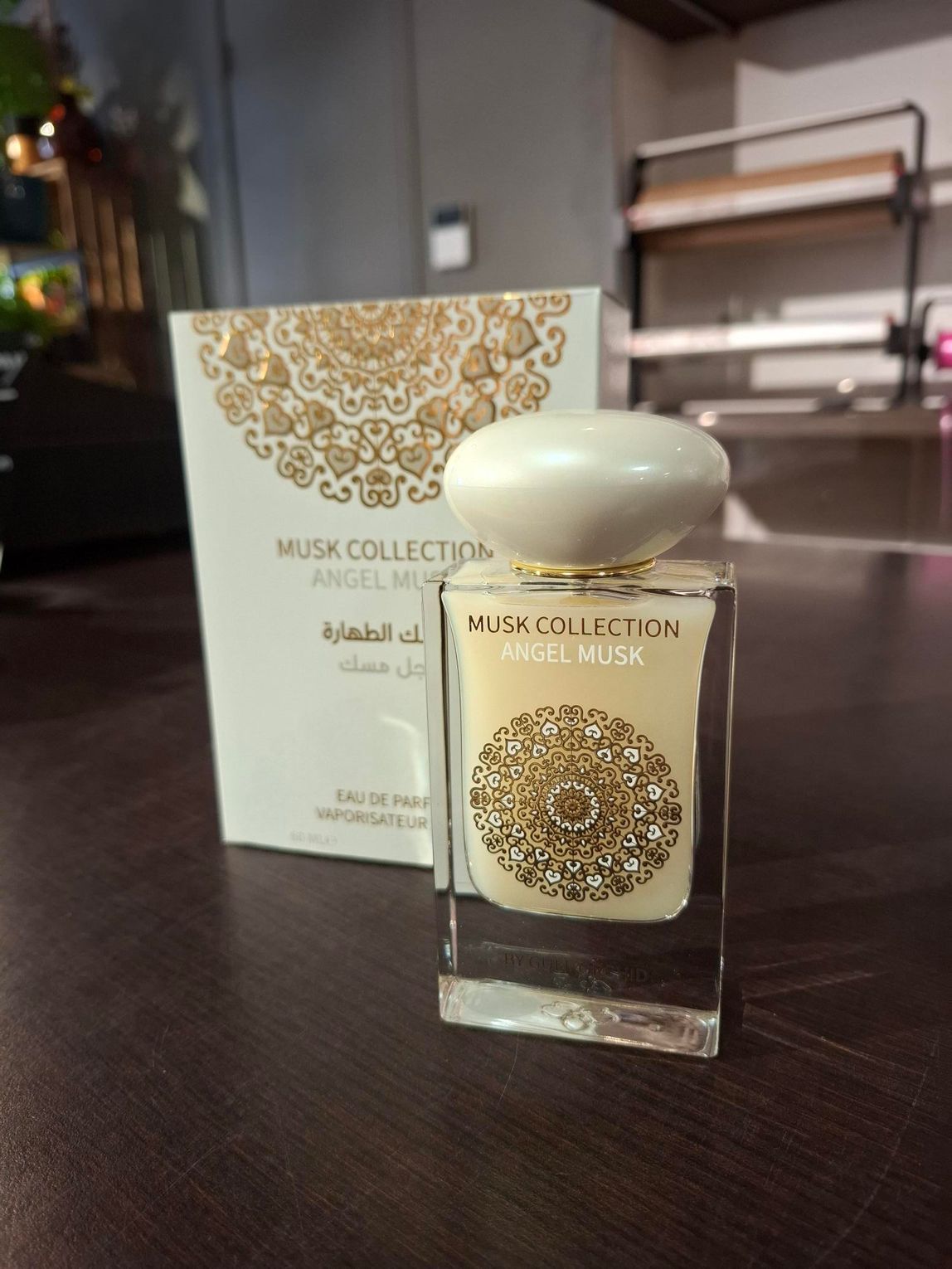 Een glazen flesje Musk Collection Angel Musk parfum met een witte dop, staand voor de bijbehorende doos.