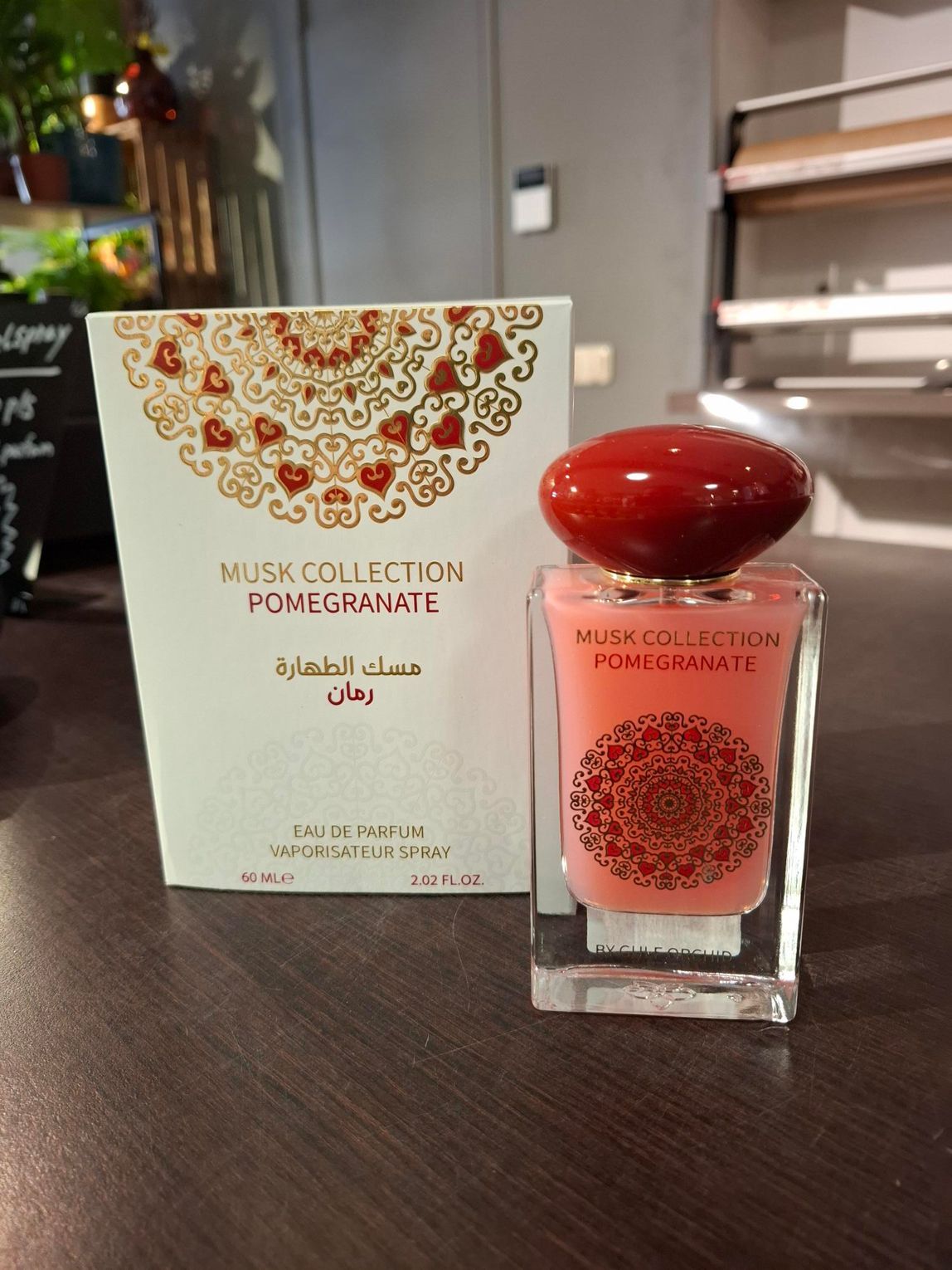 Een doos en een flesje Musk Collection Pomegranate parfum, met sierlijke rode patronen en een dieprode dop.