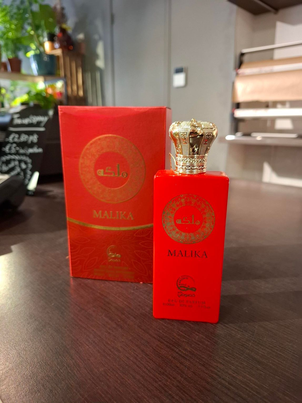 Een rode parfumfles met gouden dop staat naast een bijpassende rode doos op een tafel.
