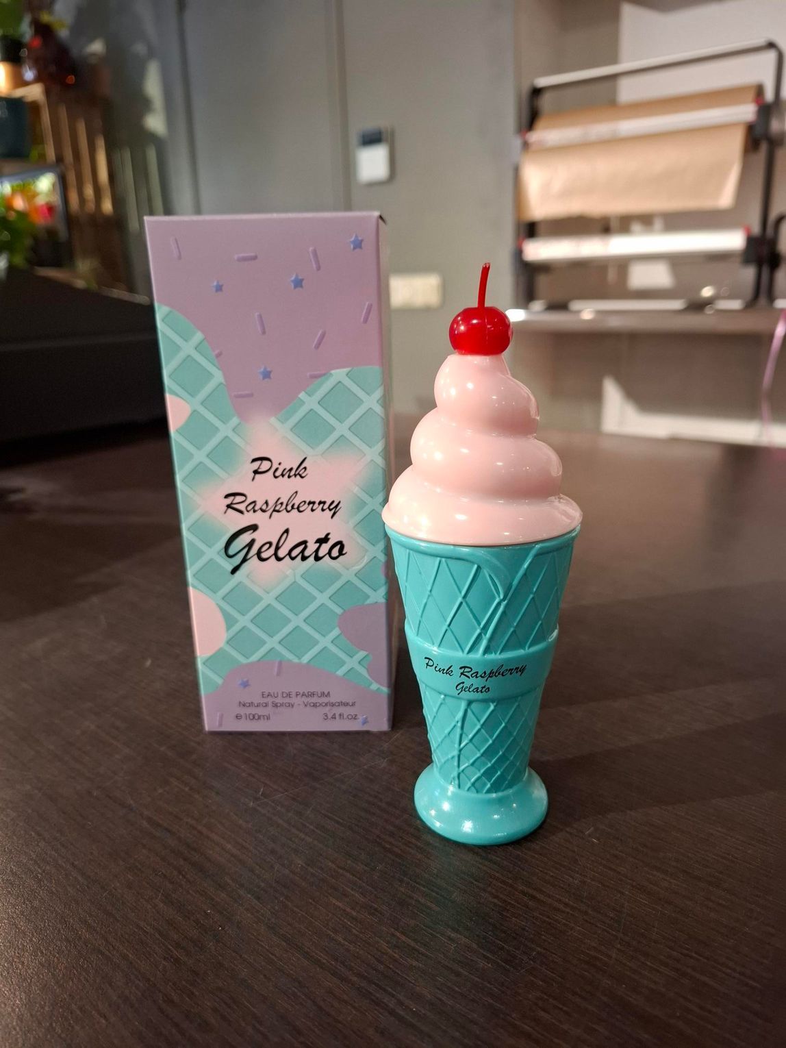 Roze softijs in een turquoise hoorntje met een kers, naast een pastelkleurig menukaartje op een tafel.