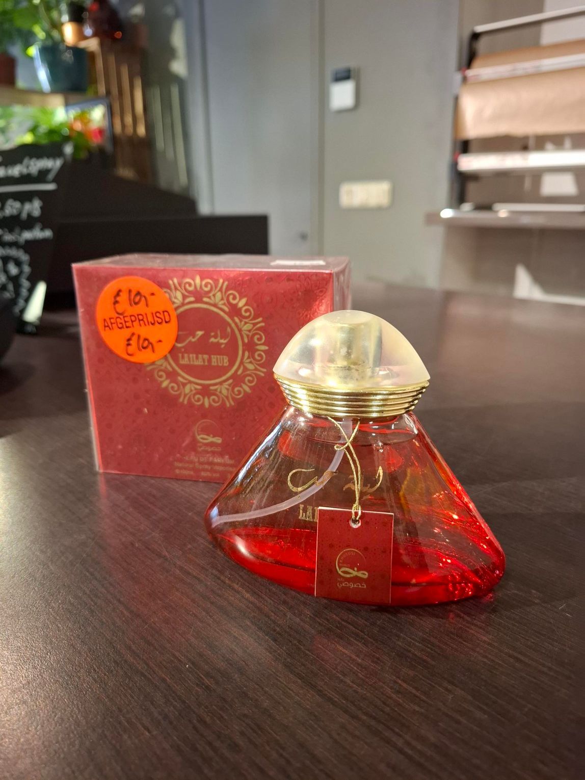 Een rode parfumfles met gouden dop staat op een donkere tafel naast de rode doos in een winkel.