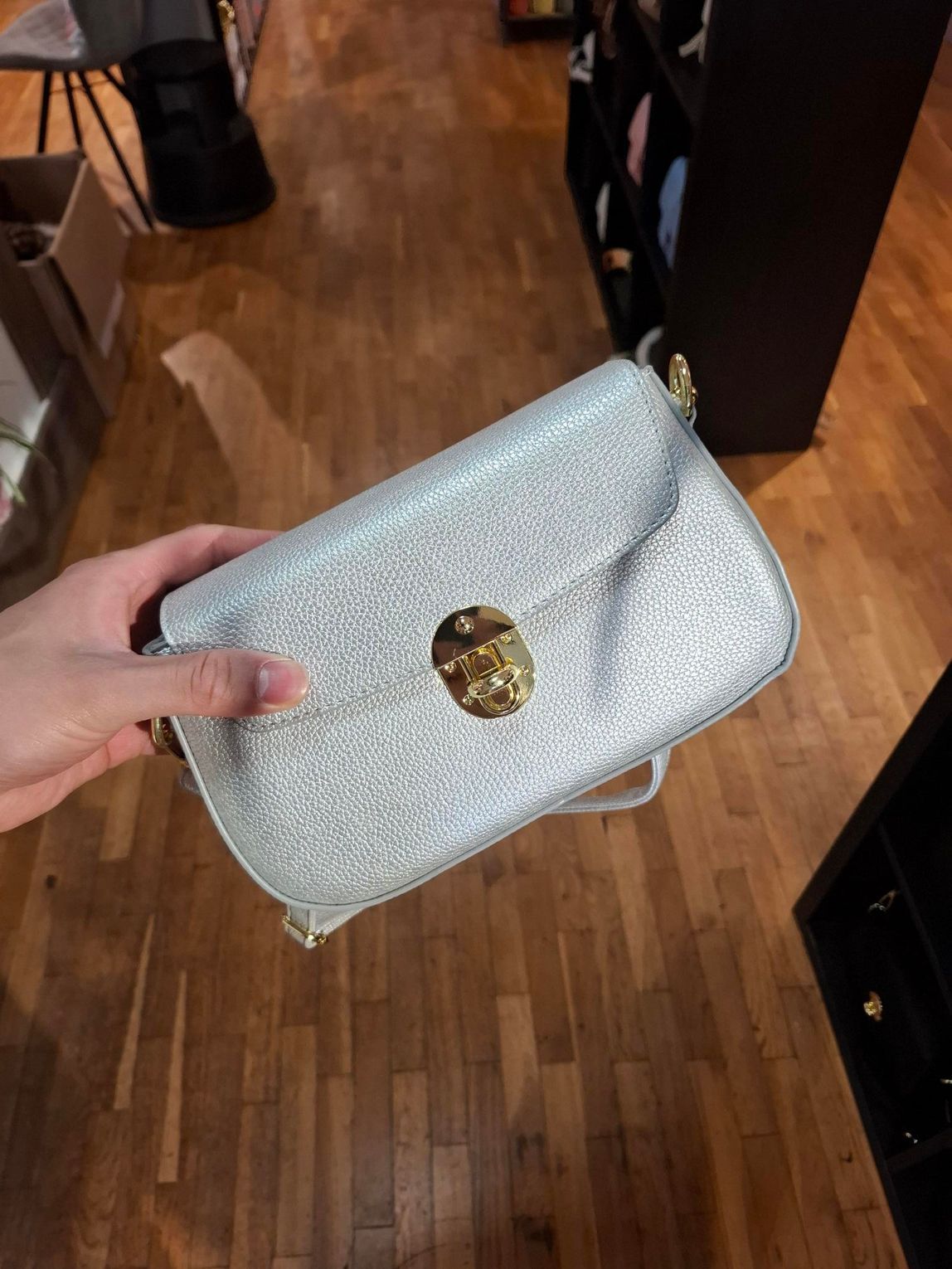 Hand die een zilveren glittertasje met een gouden sluiting vasthoudt, boven een houten vloer.
